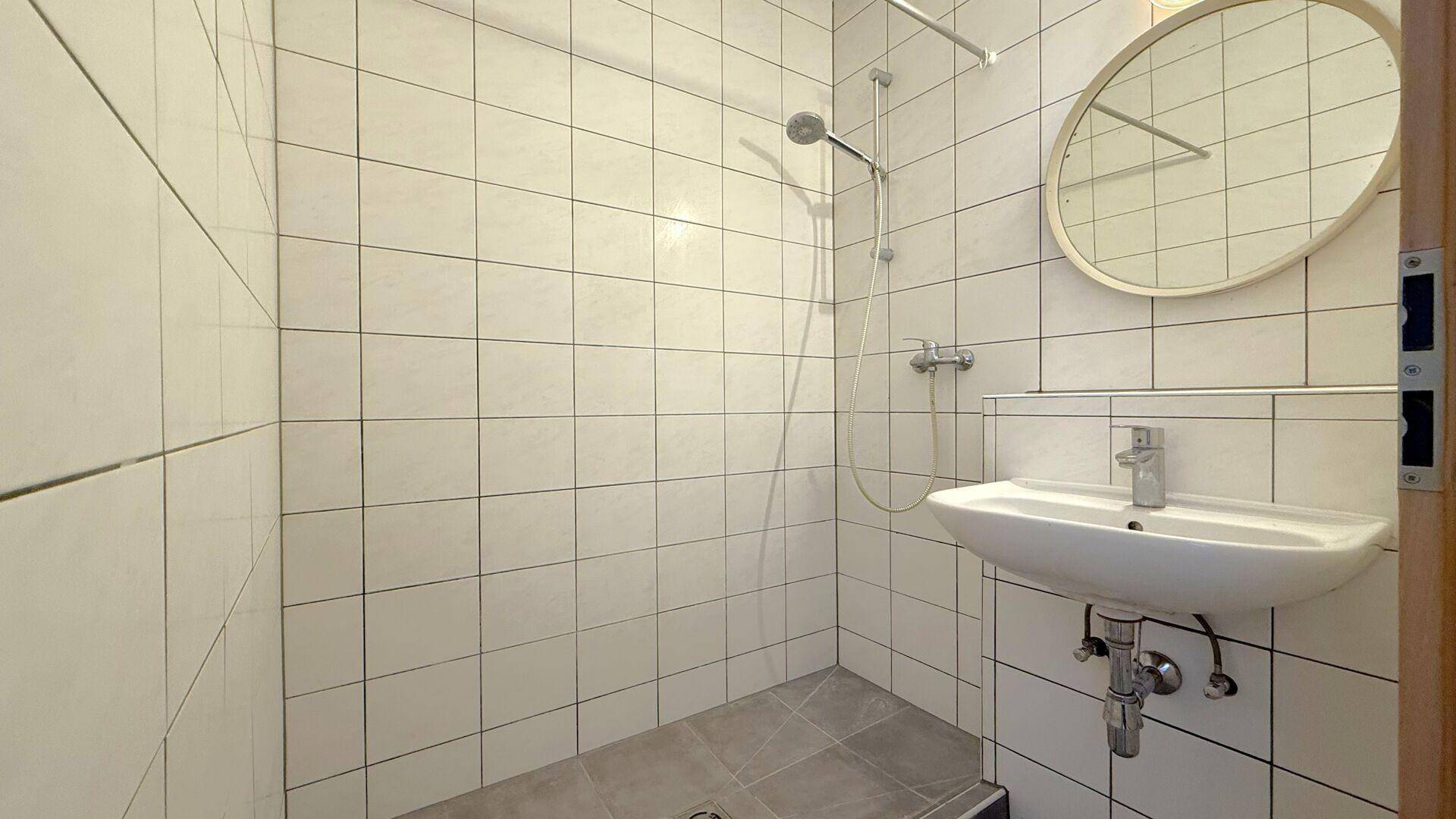 Kleines Badezimmer mit Duschbereich, Waschbecken und weißen Fliesen.
