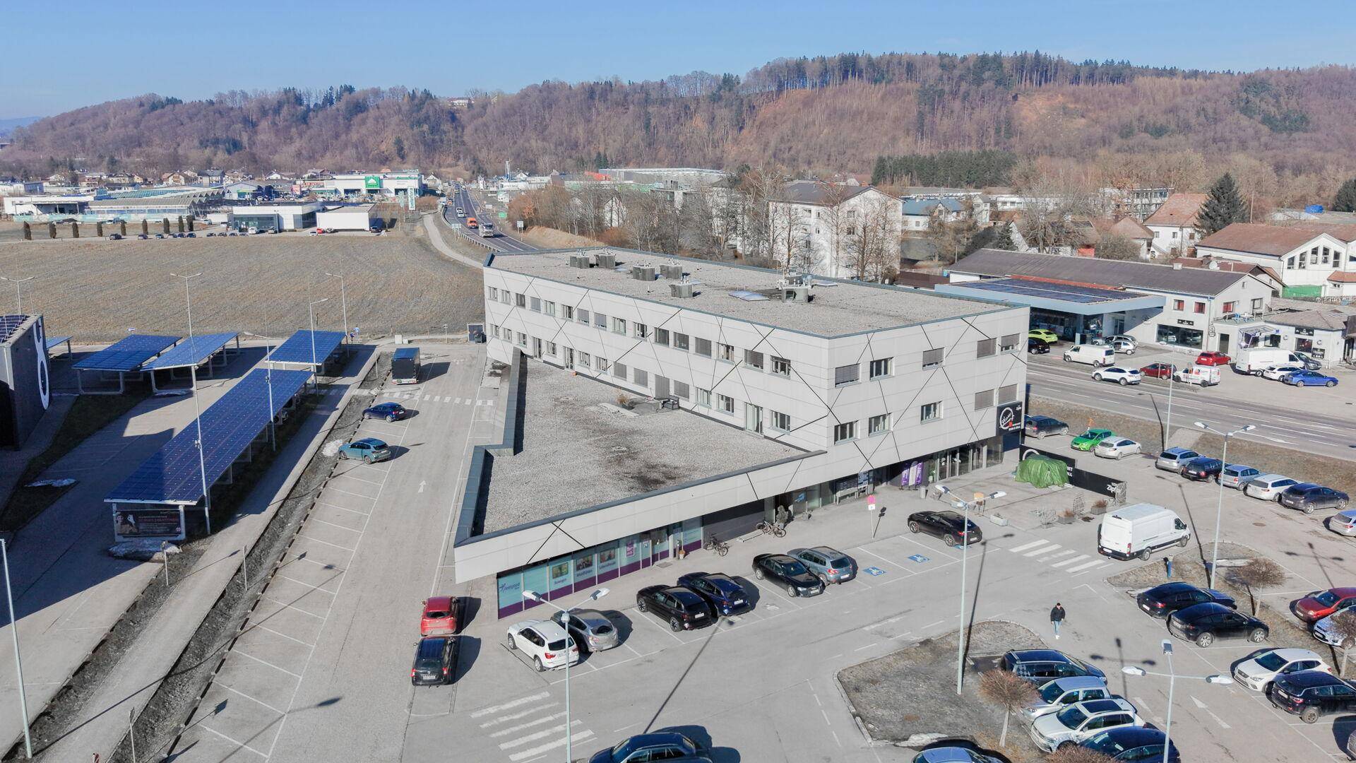Geschäftshaus mit moderner Architektur, umgeben von Parkplätzen und einer grünen Hügellandschaft.