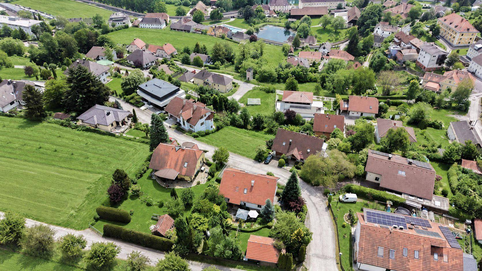 Weitläufige Luftaufnahme einer Wohnsiedlung mit Häusern, Gärten, Straßen und einem kleinen Teich.