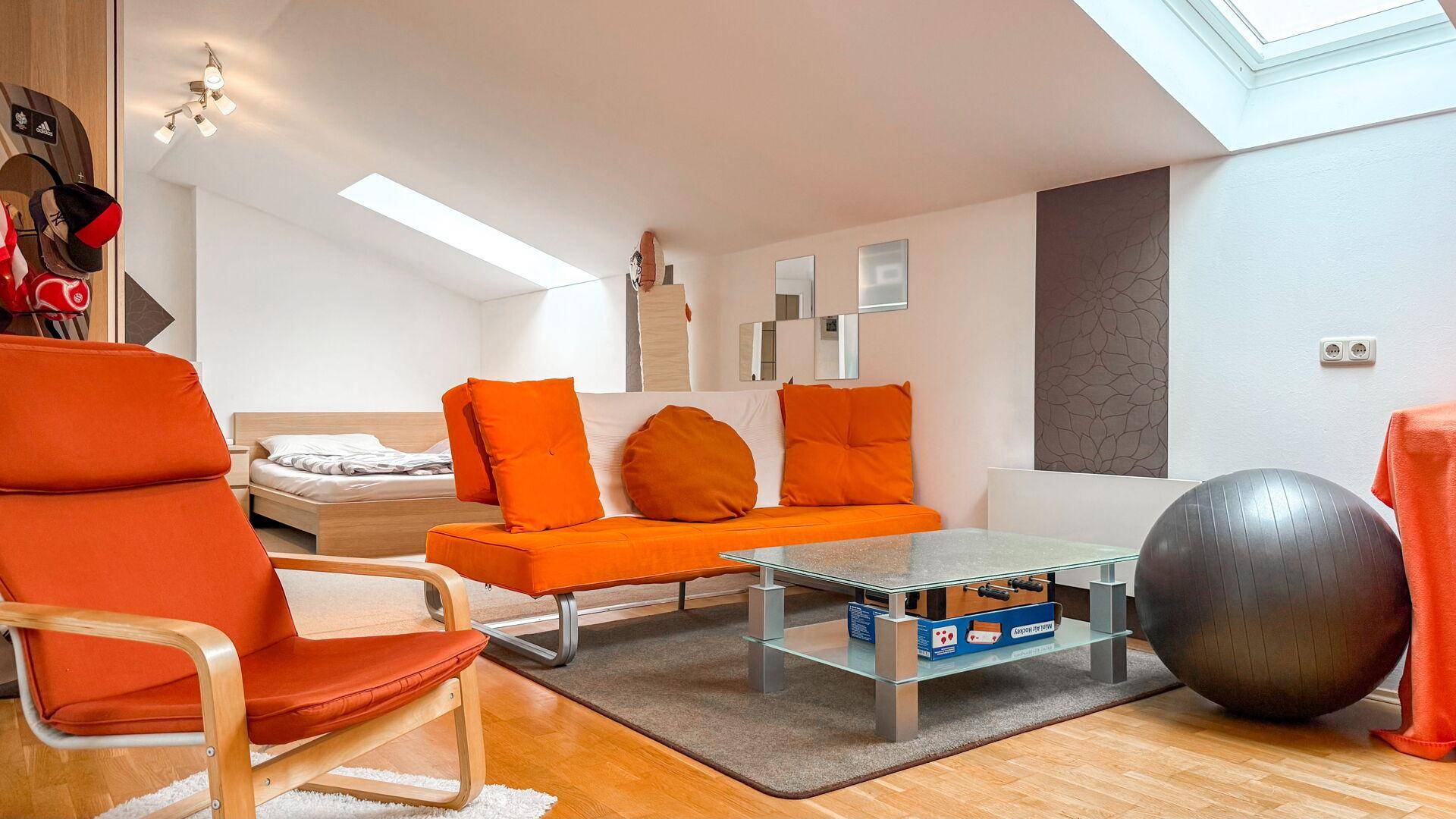 Dachgeschoss-Wohnraum mit Schrägen, orangefarbenen Möbeln und Holzboden.