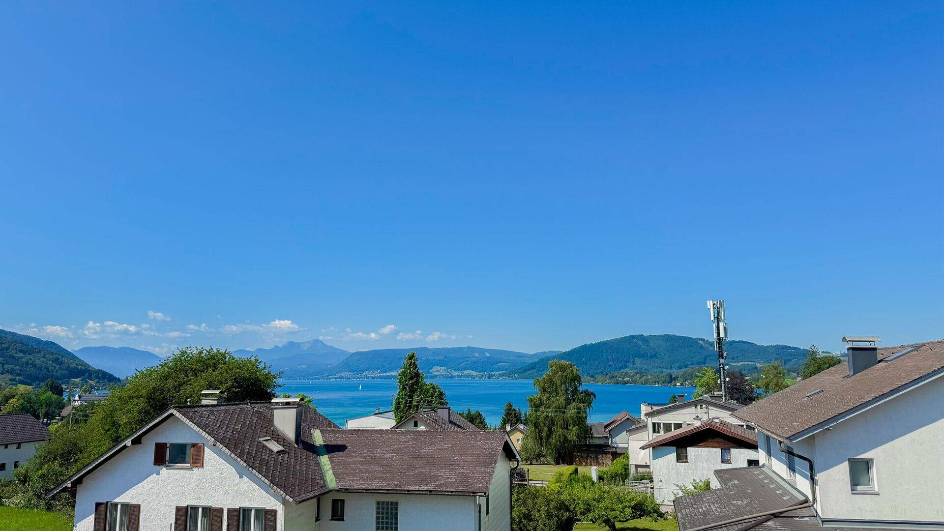 Weitläufiger Blick auf den glitzernden See und die majestätischen Berge unter blauem Himmel.