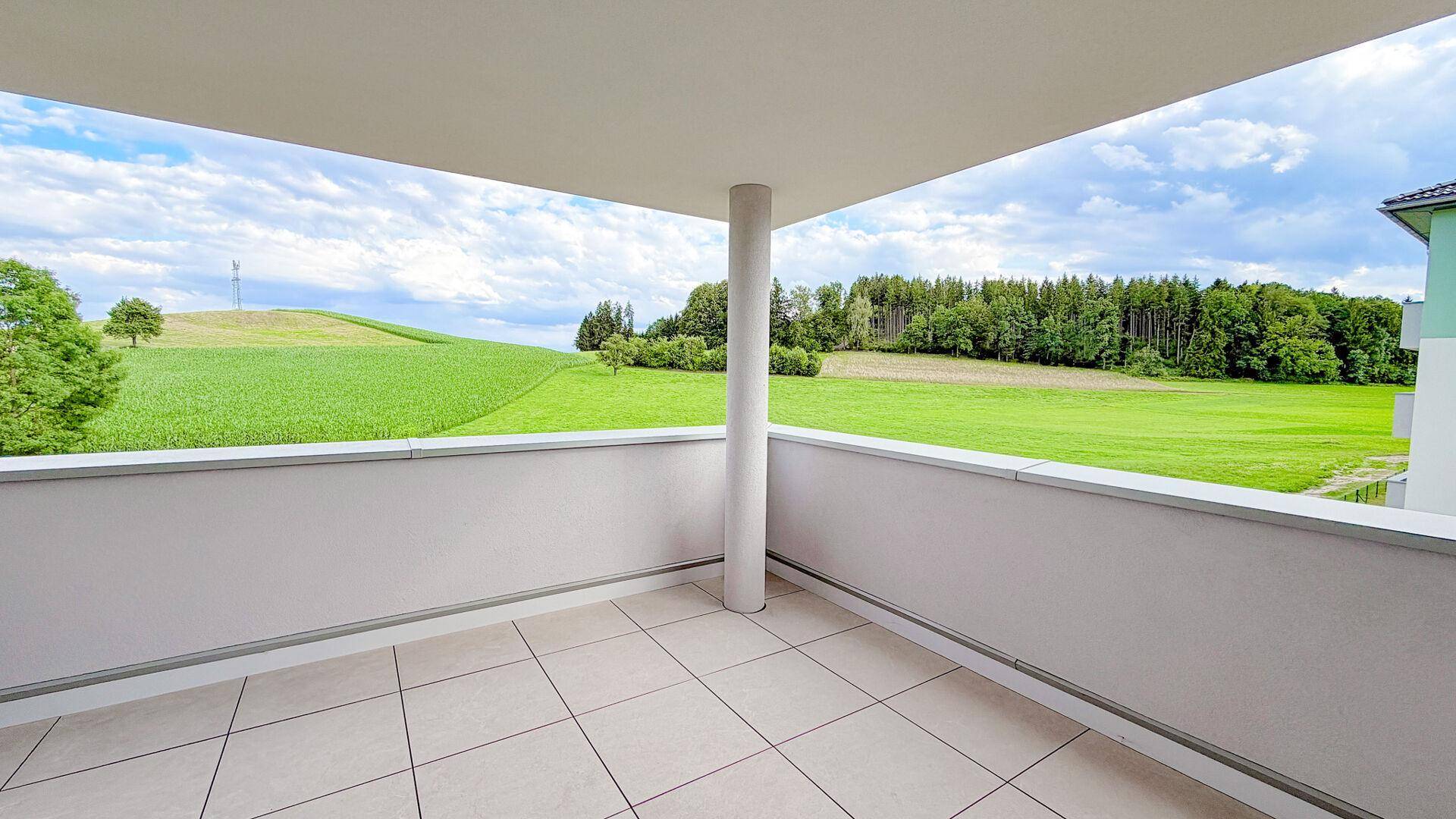 Überdachter Balkon mit Fliesenboden und weitem Blick auf die umliegende grüne Landschaft.