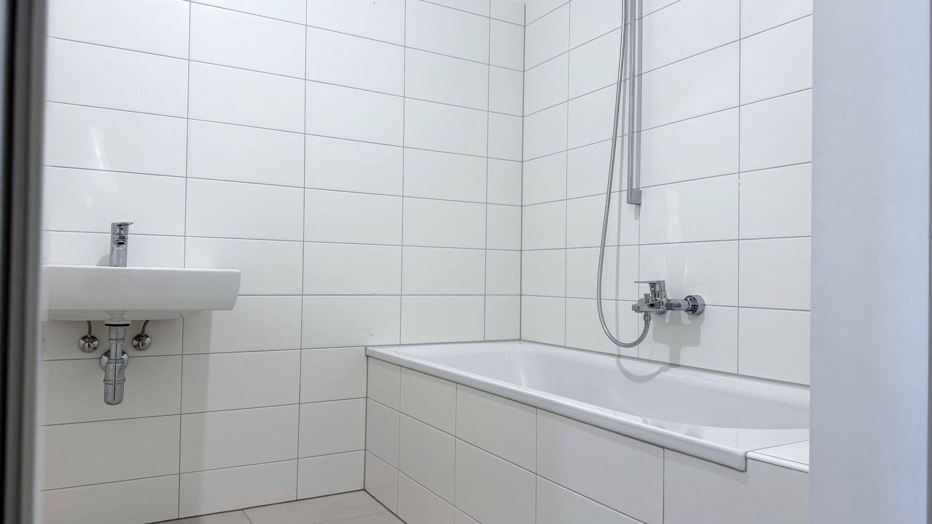 Modernes Badezimmer mit weißen Fliesen, einer Badewanne mit Duschfunktion und einem Waschbecken.