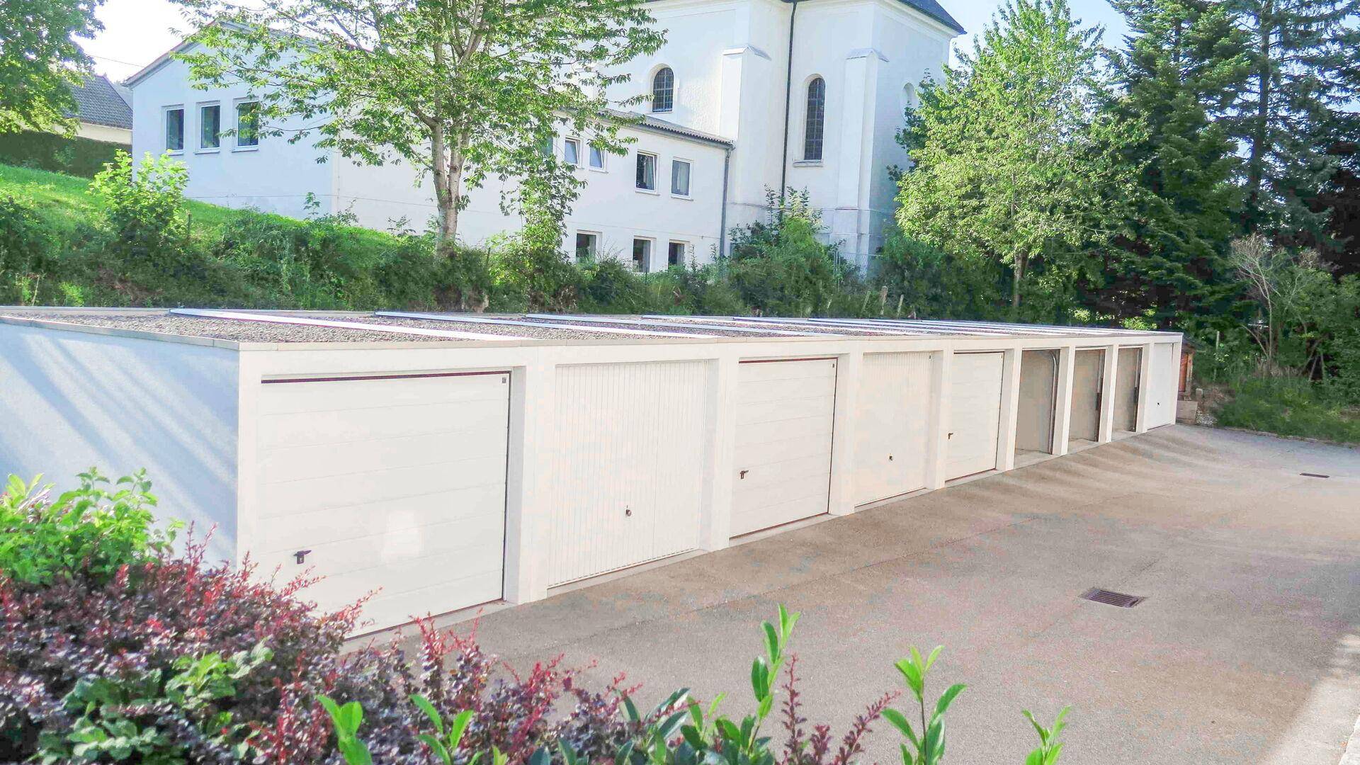 Reihe von Garagenboxen neben einem Gebäude mit viel Grünfläche.