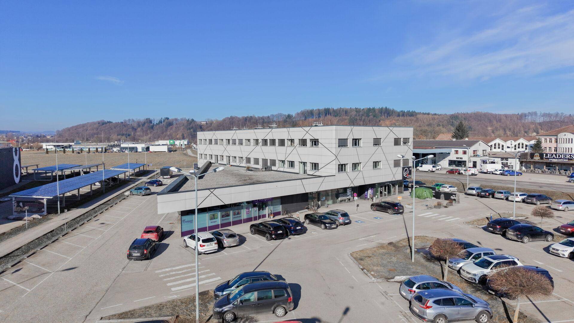 Modernes Geschäftsgebäude mit Parkplätzen und umliegender Infrastruktur unter blauem Himmel.