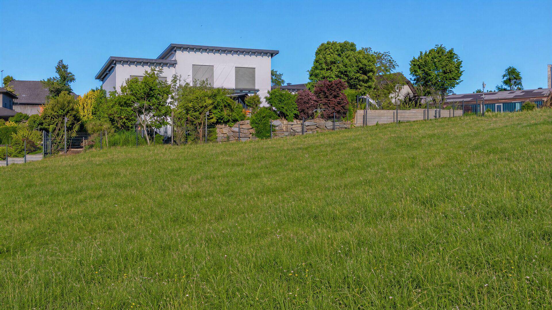 Modernes Wohnhaus mit Flachdach und gepflegter Gartenanlage auf einem Hanggrundstück.