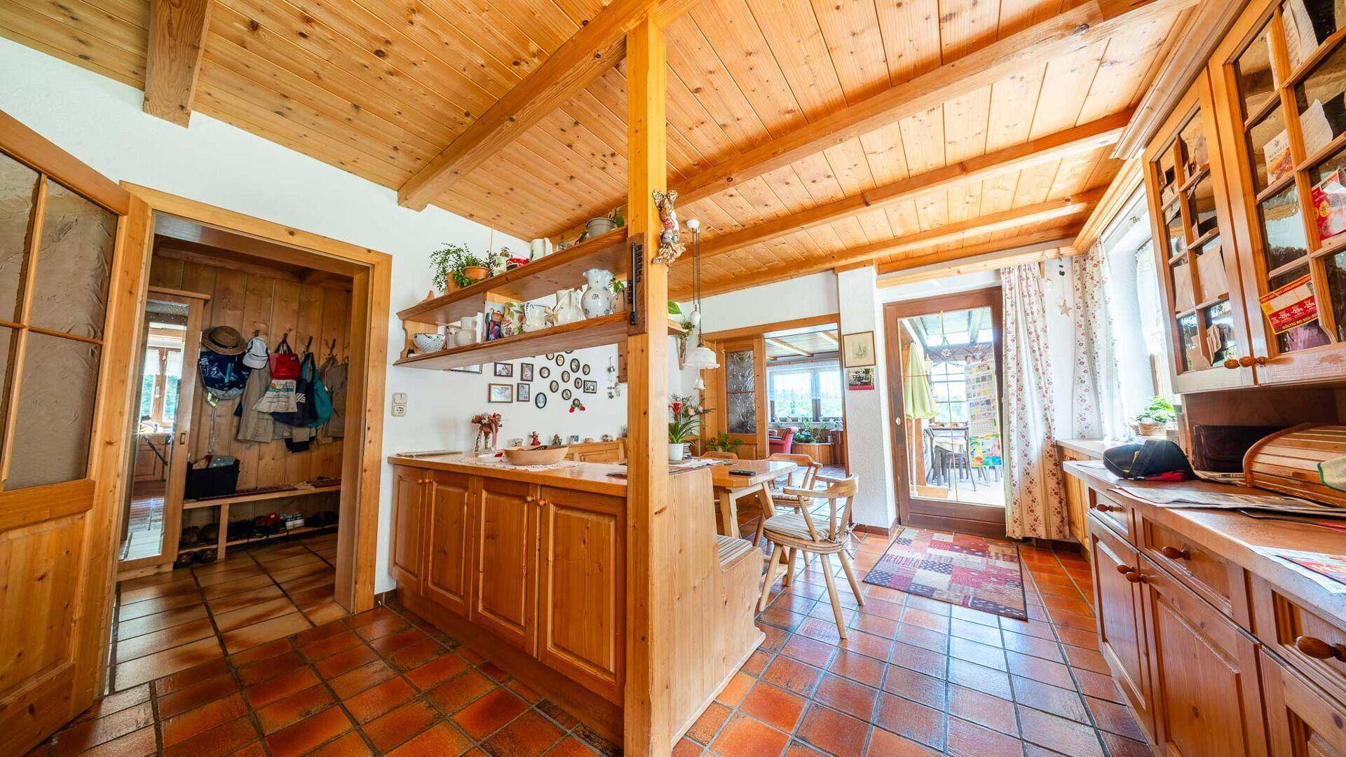 Rustikale Küche mit Holzschränken, Terrakottafliesen und offenem Zugang zum Essbereich.