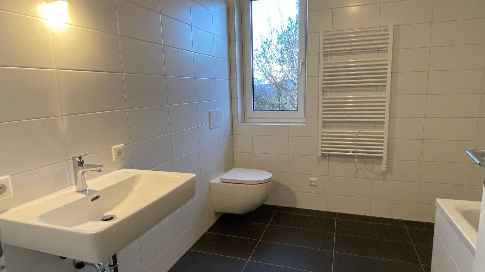 Modernes Badezimmer mit Wand-WC, Waschbecken, beheiztem Handtuchhalter und Fenster.