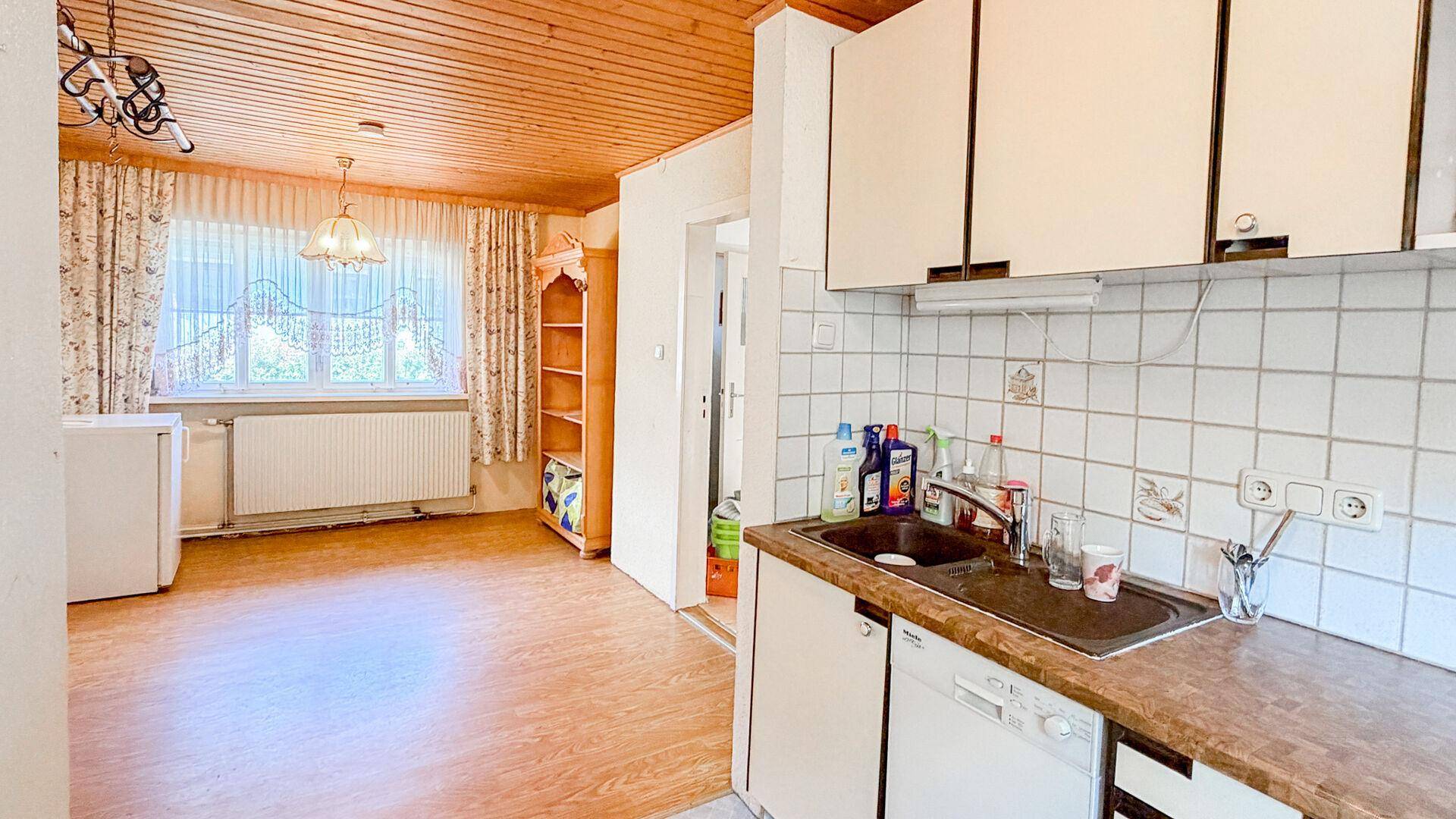 Küche mit weißen Hängeschränken, Spülbecken und Blick in einen angrenzenden Wohnbereich.