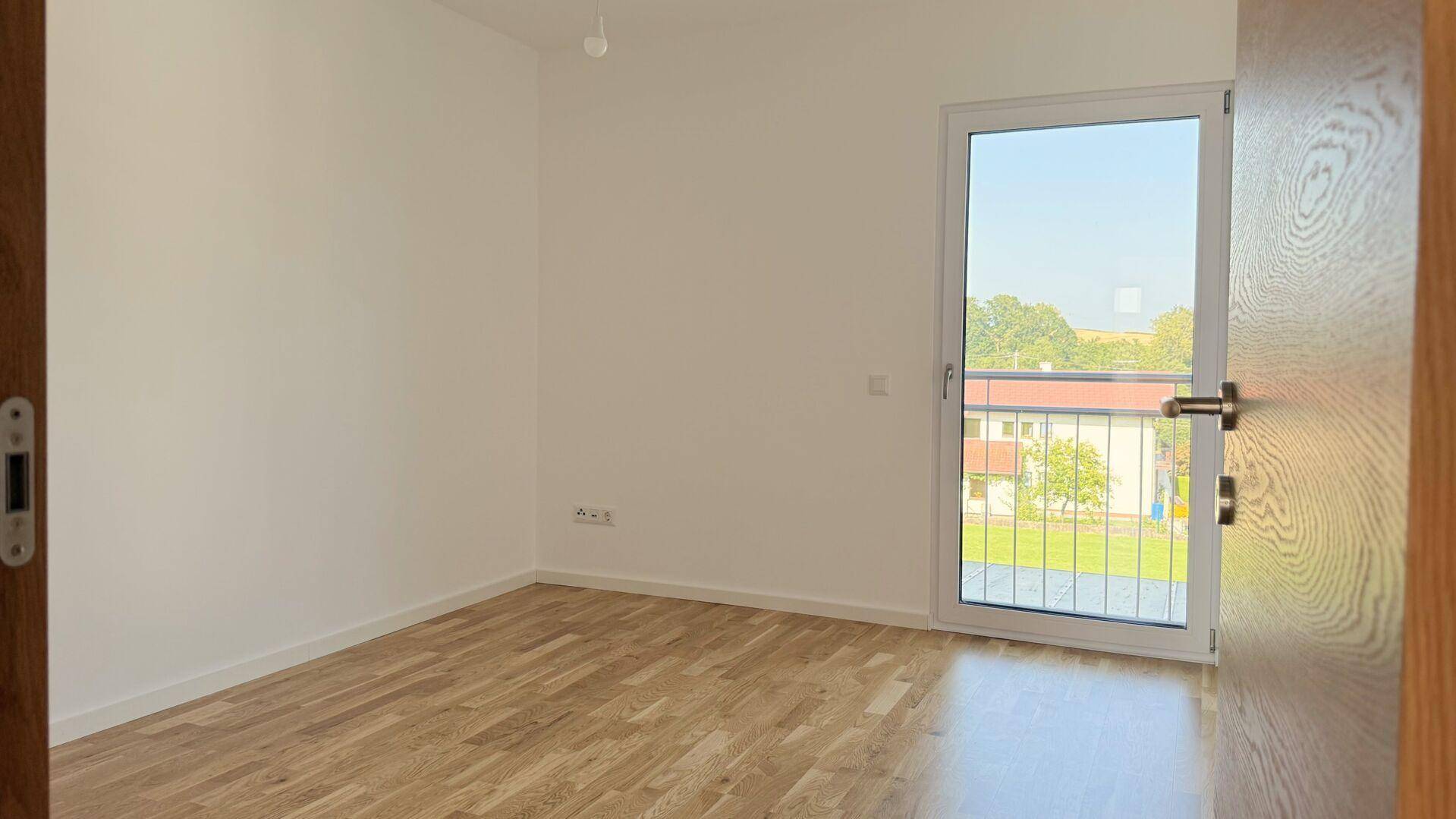 Leeres Zimmer mit Holzboden und einem französischen Balkon, der einen weiten Blick bietet.