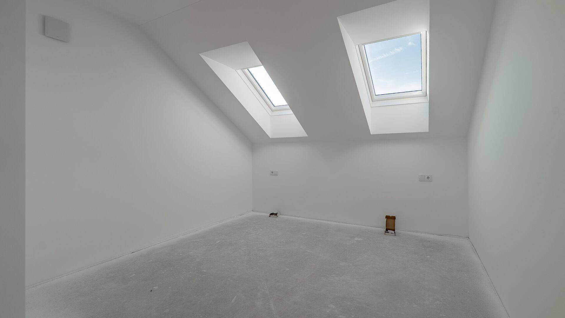 Unfertiges Schlafzimmer mit schrägen Wänden und zwei Dachfenstern für viel natürliches Licht.