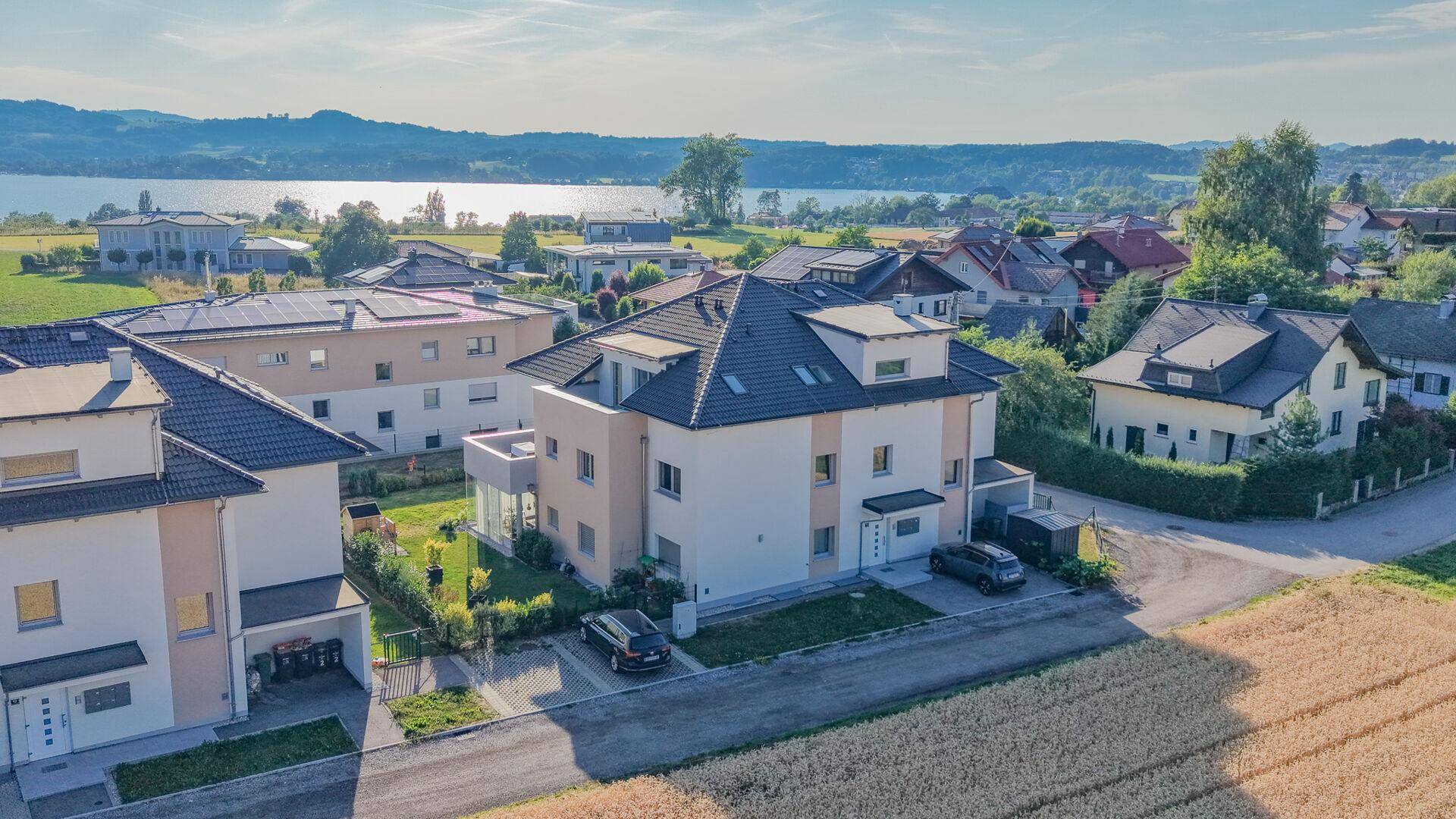 Luftaufnahme einer Wohnanlage mit Seeblick, umgeben von Feldern und weiteren Häusern.