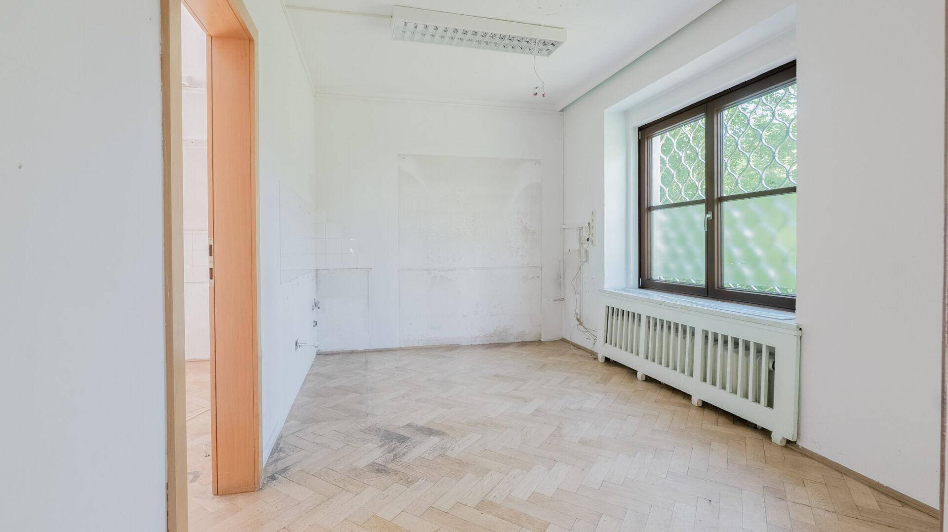 Leerer Raum mit Fischgrätparkett, Fenster und Heizkörper, ideal als Büro oder Schlafzimmer.