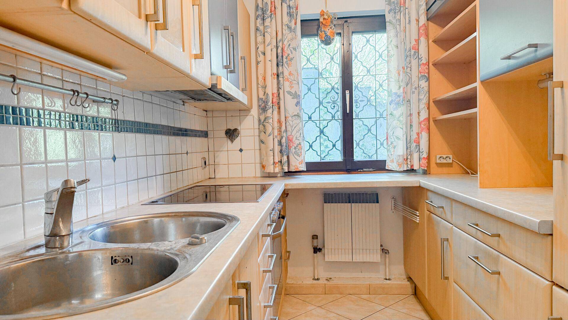 Küche mit Doppelspüle, Kochfeld und Holzschränken, gut belichtet durch ein Fenster.