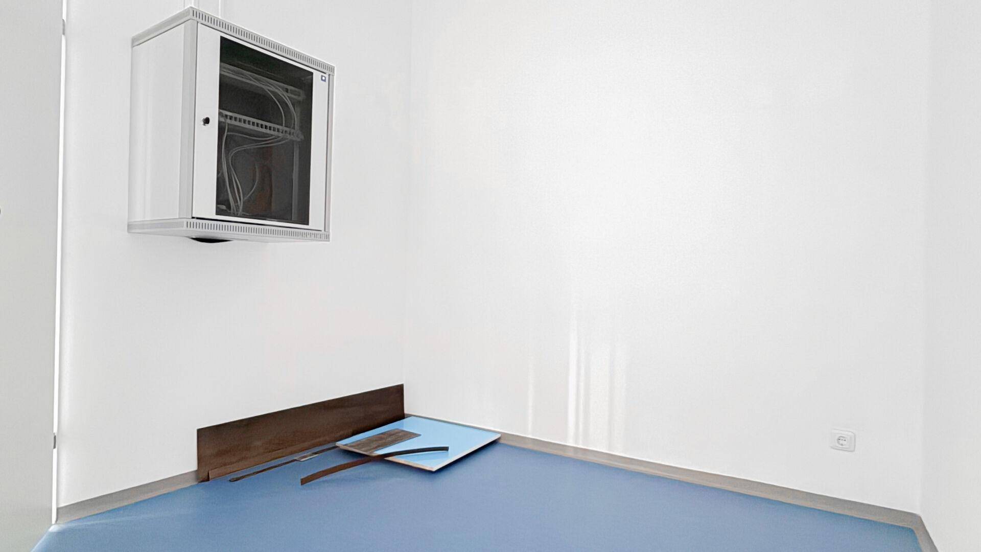 Technischer Raum mit Serverschrank und blauem Boden, ideal für IT-Infrastruktur oder Lagerung.