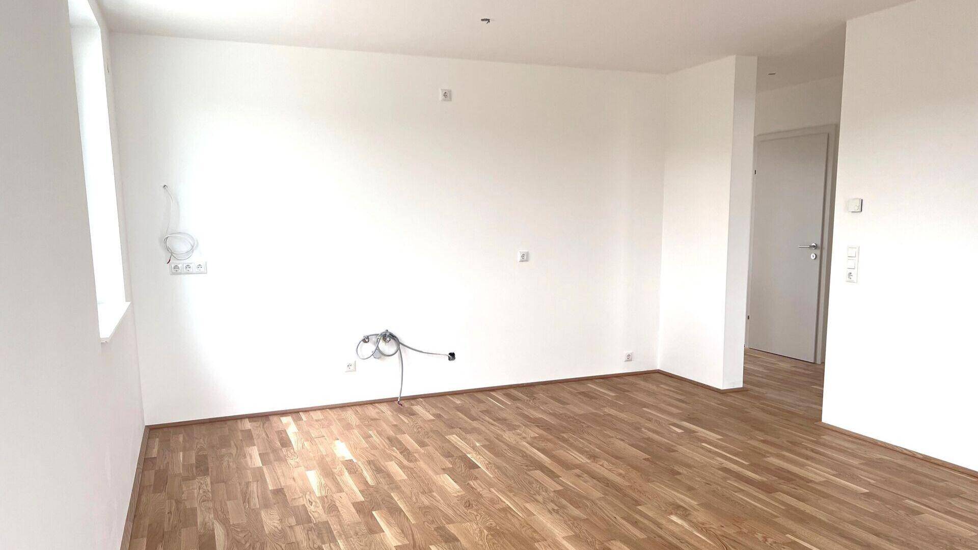 Leeres Wohnzimmer mit hellem Parkettboden und weißen Wänden, bereit für die Einrichtung.