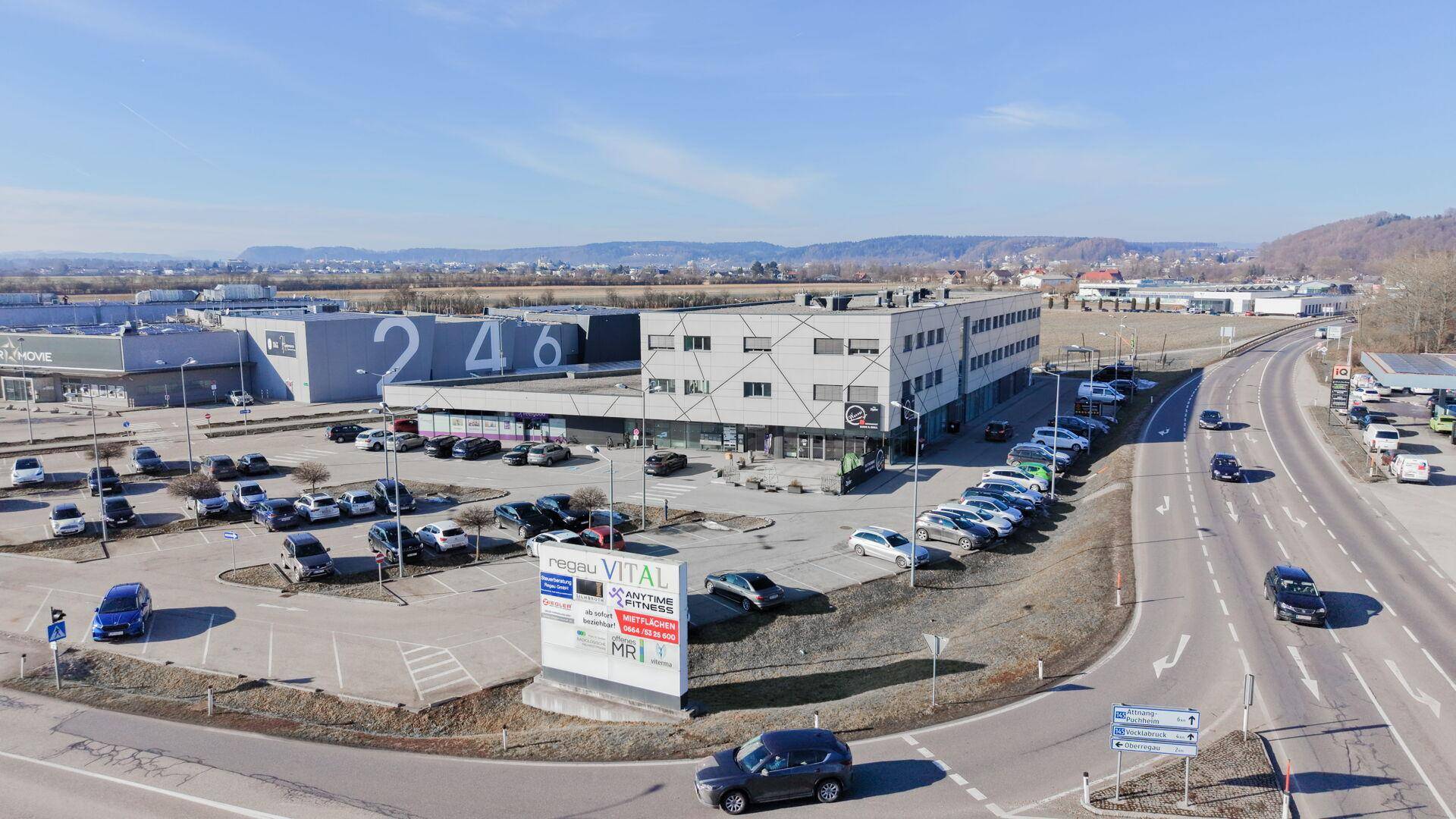 Luftaufnahme eines modernen Geschäftsgebäudes mit großem Parkplatz und umliegender Infrastruktur.