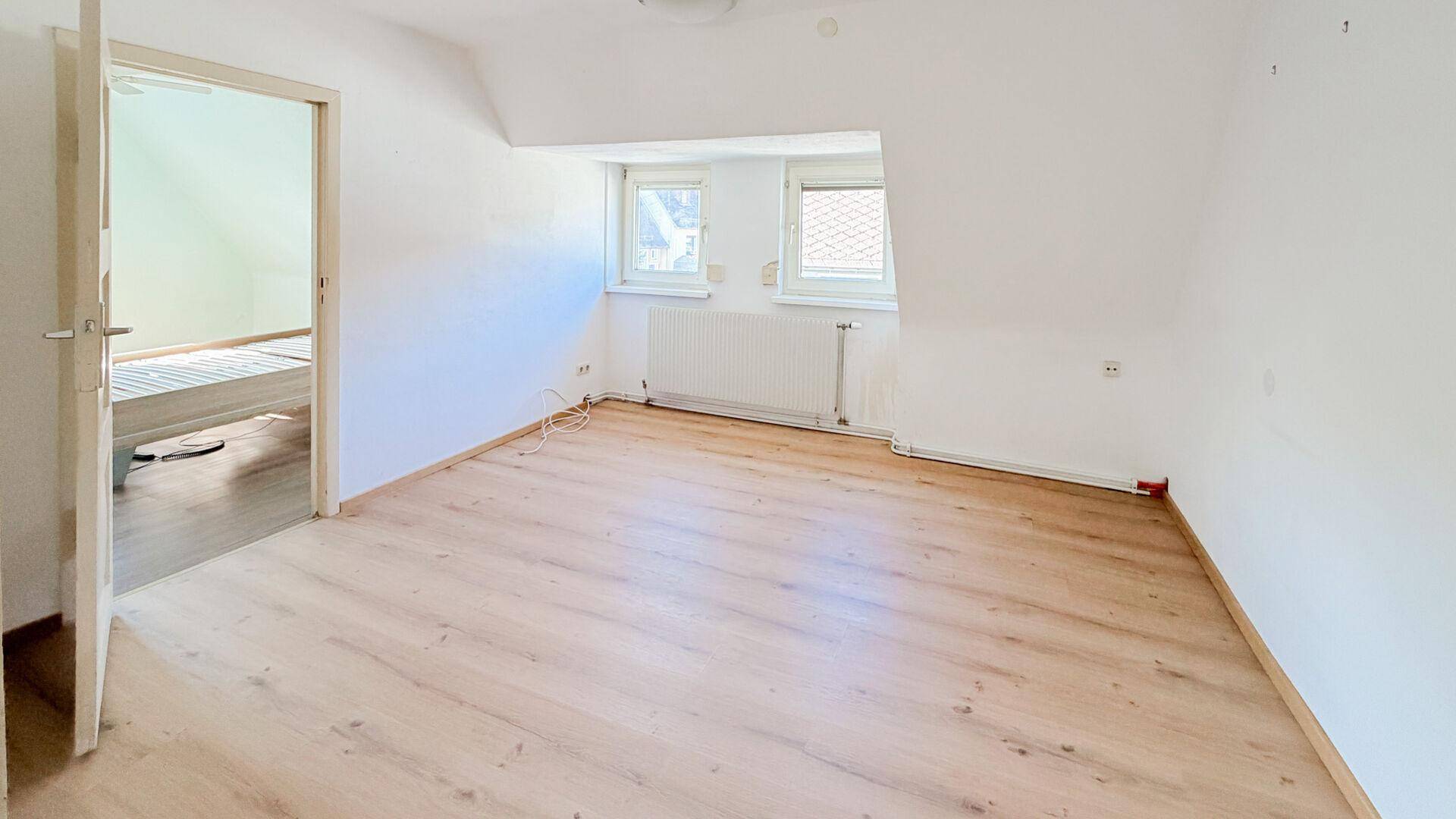 Helles Schlafzimmer im Dachgeschoss mit Laminatboden, weißen Wänden und zwei Fenstern.
