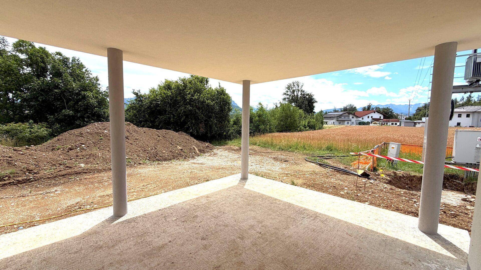 Überdachte Terrasse im Rohbauzustand mit Blick auf die Baustelle und die ländliche Umgebung.