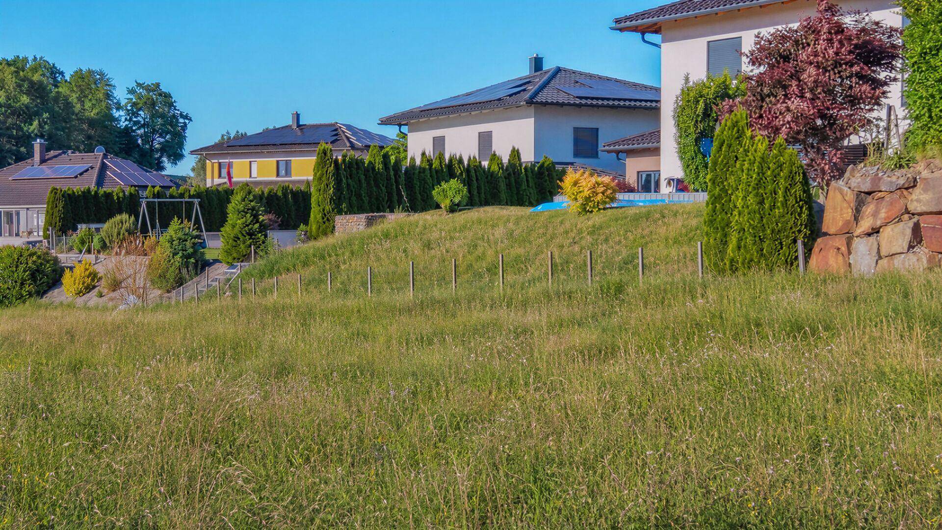 Hanglage mit weitem Blick über grüne Wiesen und benachbarte Wohnhäuser.