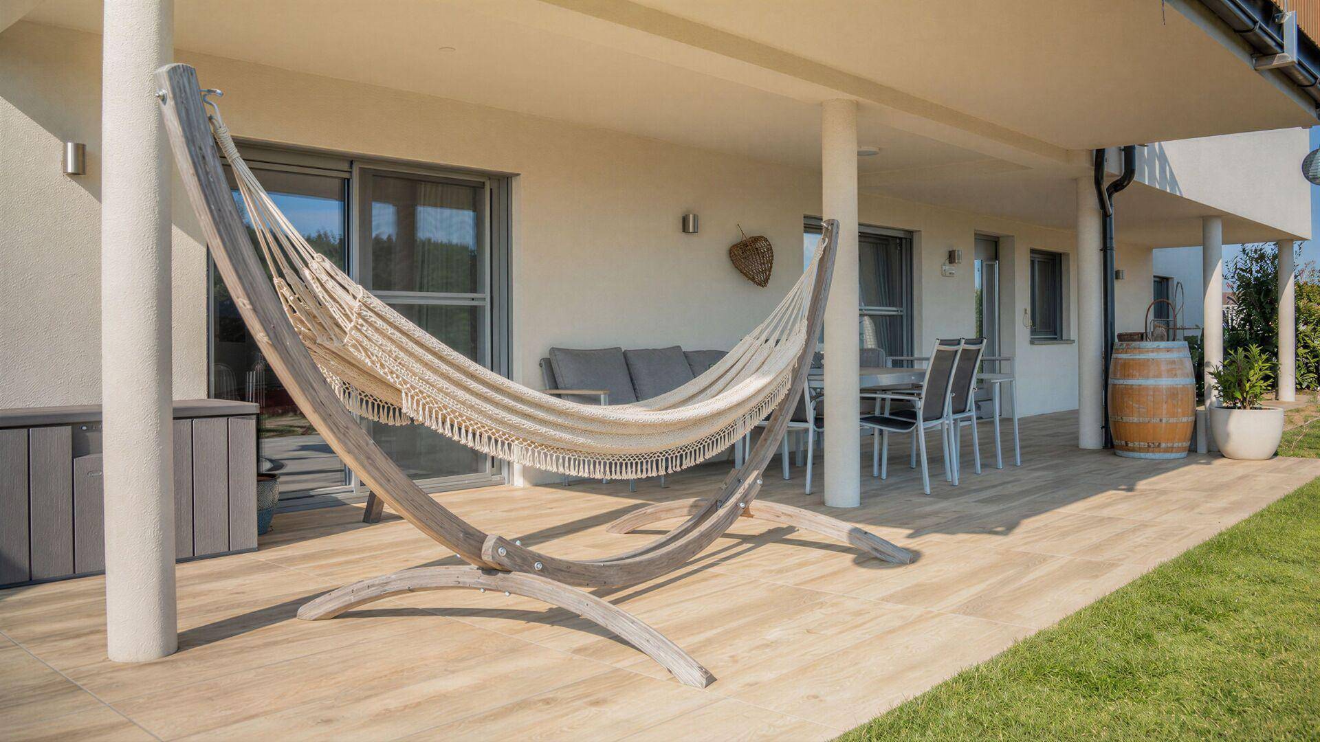 Überdachte Terrasse mit Hängematte, Gartenmöbeln und Fliesenboden, ideal zum Entspannen.