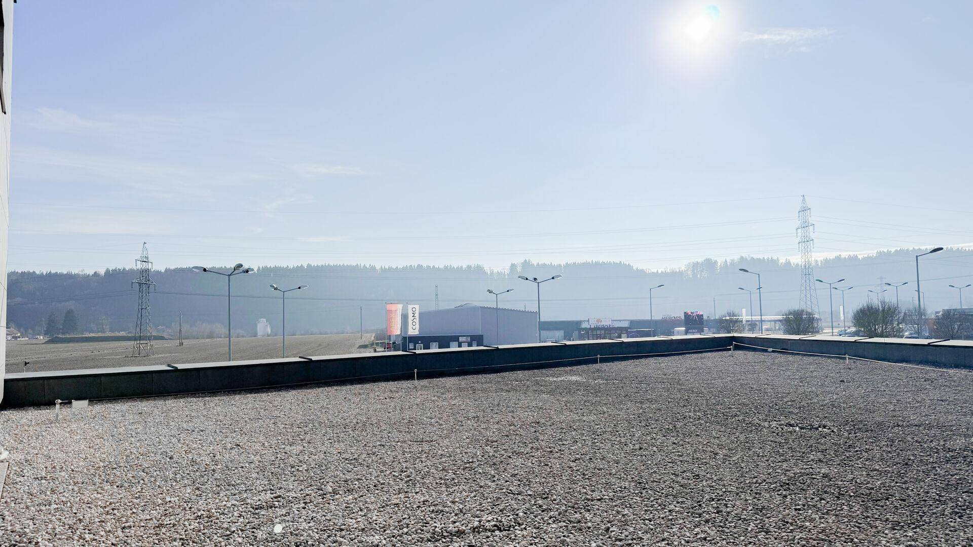 Weitläufige Dachfläche mit Kiesbelag und Blick auf die umliegende Landschaft und Industriegebäude.