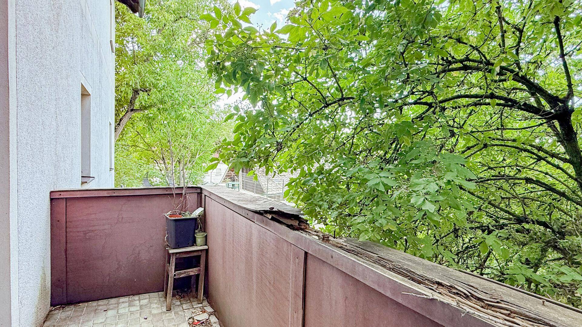 Kleiner Balkon mit einfacher Einrichtung und üppigem Grünblick von Bäumen umgeben.
