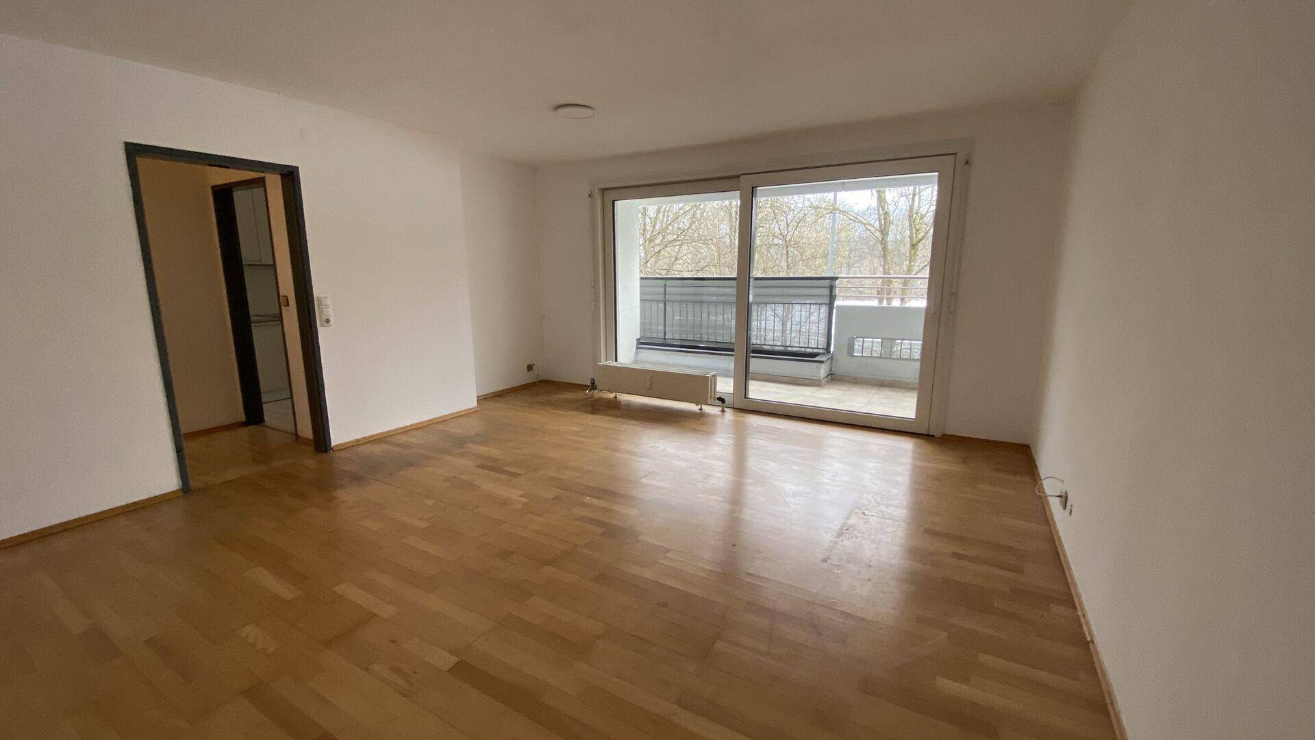 Geräumiges Wohnzimmer mit Holzboden, großen Fenstern und Zugang zu einem weiteren Raum.