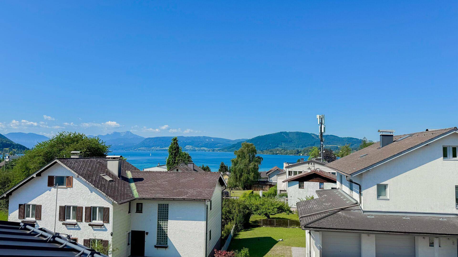 Malerischer Blick auf den See und die umliegenden Berge über den Dächern der Häuser.