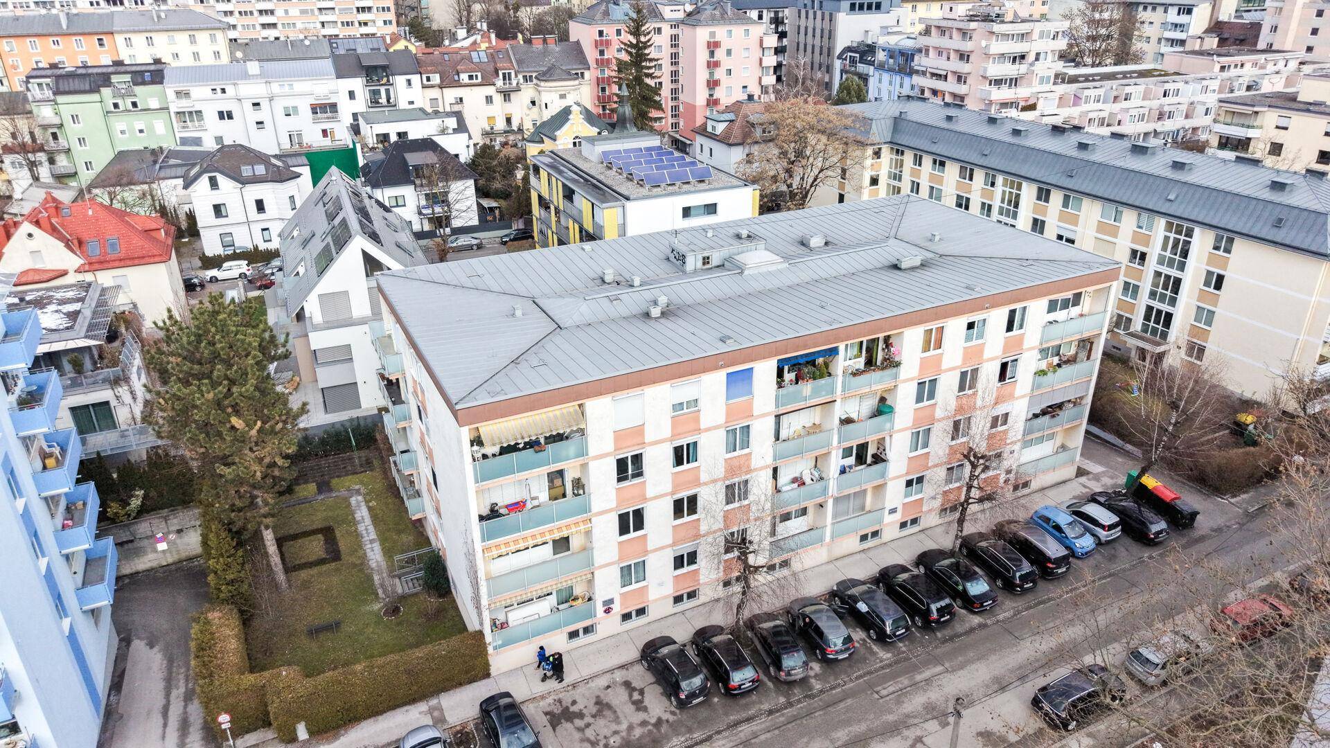 Luftaufnahme eines Wohngebäudes mit umliegenden Häusern, Bäumen und Parkplätzen.