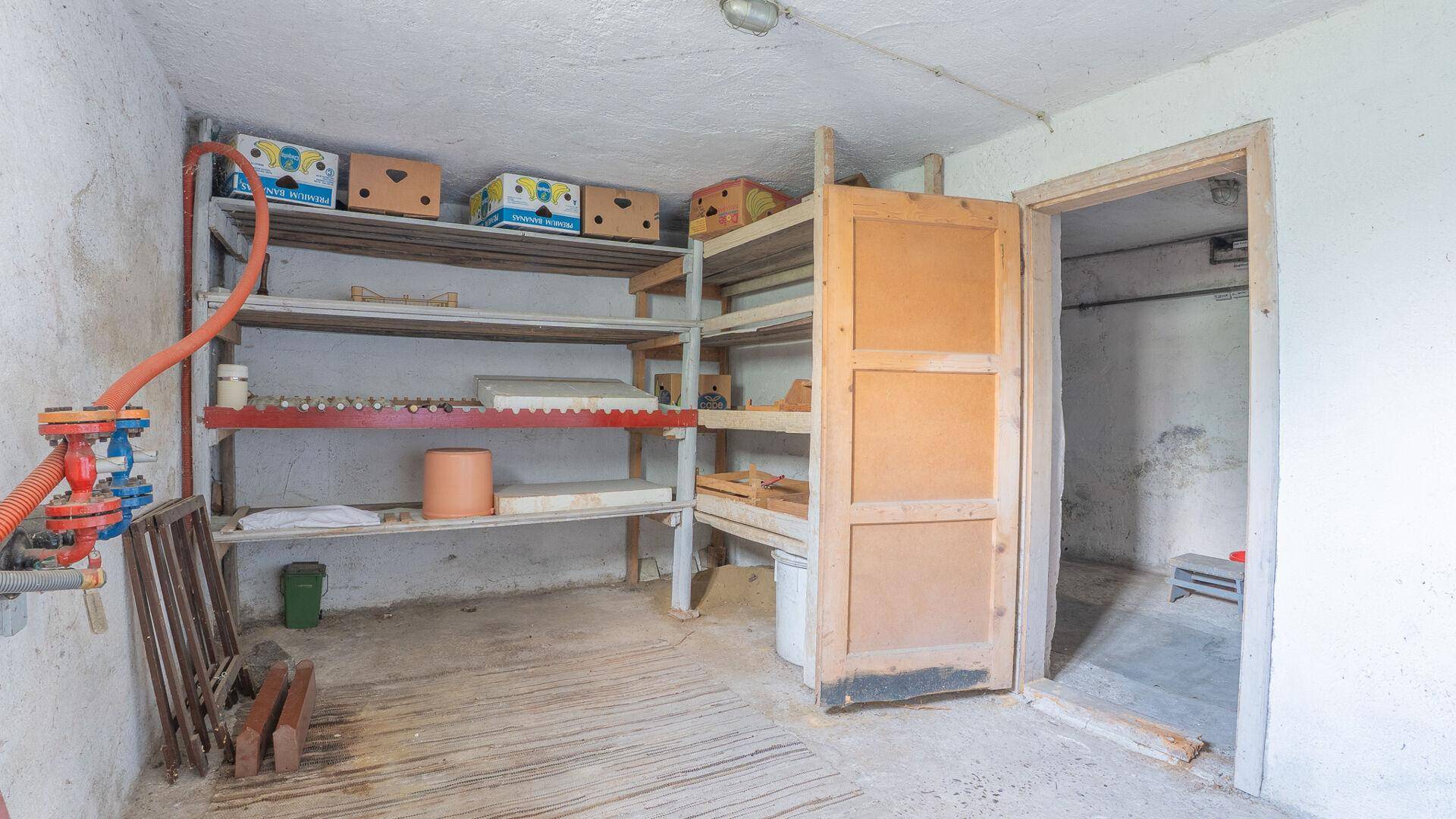 Kellerraum mit Regalen für Lagerung und Zugang zu einem weiteren Bereich.