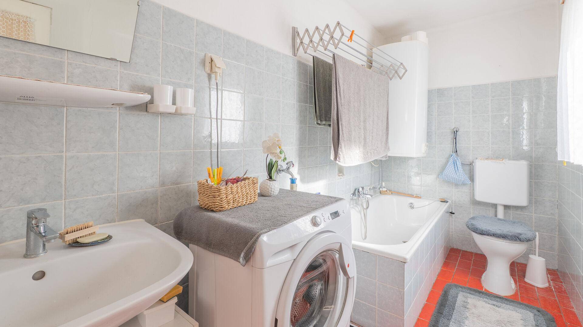 Badezimmer mit Badewanne, Waschmaschine und WC, in hellblauen Fliesen.