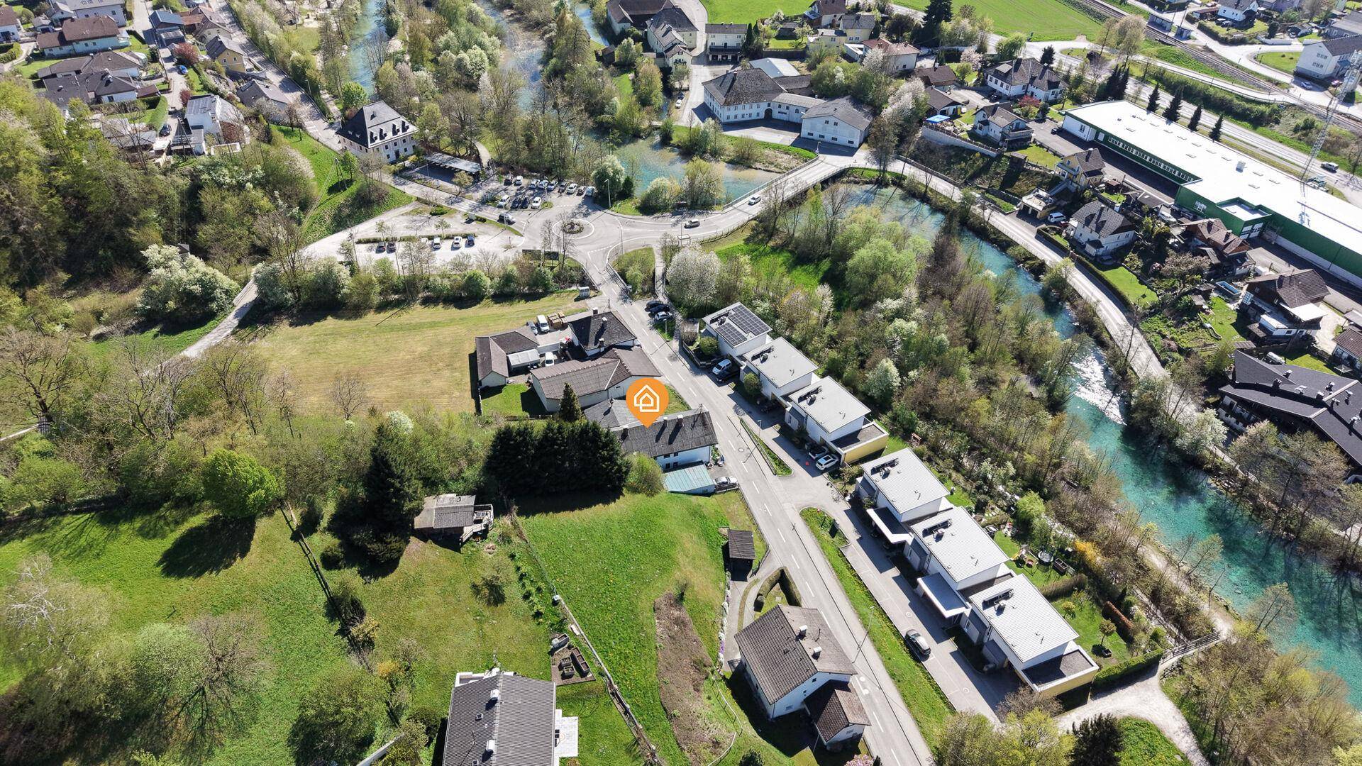 Weitläufige Luftaufnahme der Wohngegend mit Fluss, umgeben von viel Grün und weiteren Häusern.