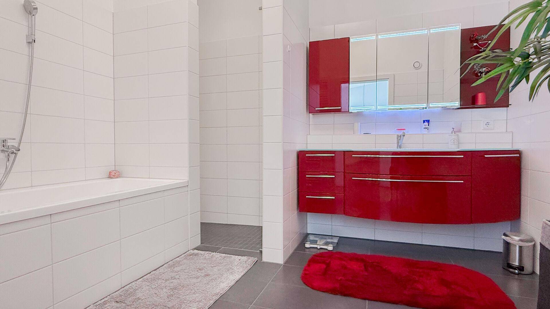 Geräumiges Badezimmer mit Badewanne, modernem roten Waschtisch und großem Spiegelschrank.