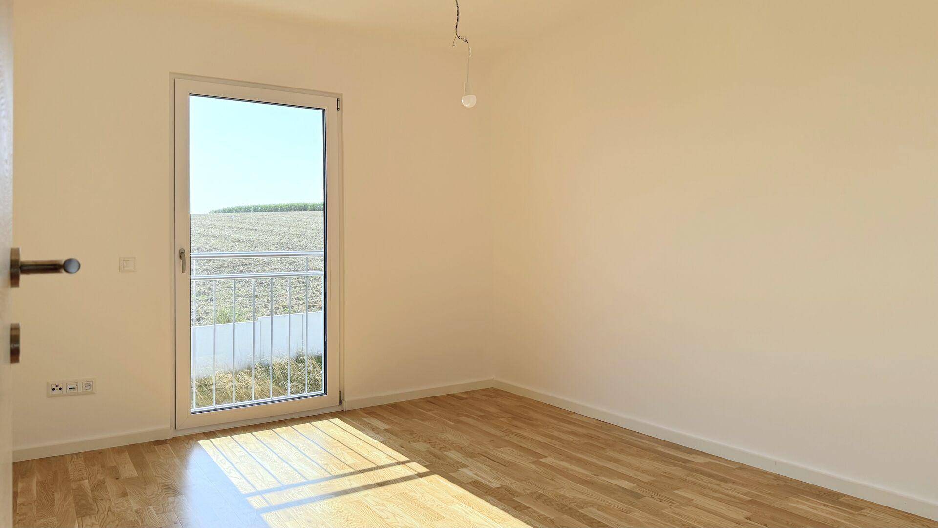 Helles Zimmer mit Parkettboden und französischem Balkon mit Blick auf die umliegende Landschaft.