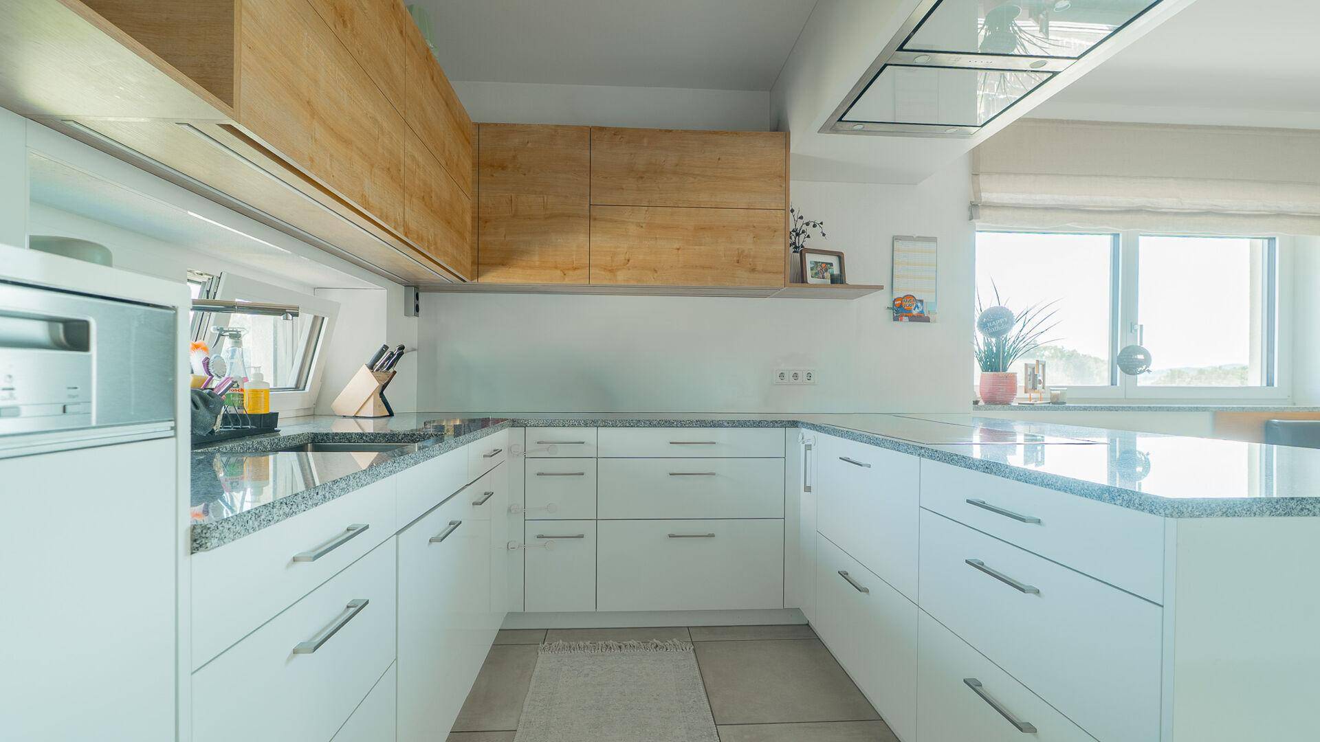 Helle Einbauküche mit weißen Schränken, Holzdetails und modernen Geräten, sehr funktional.