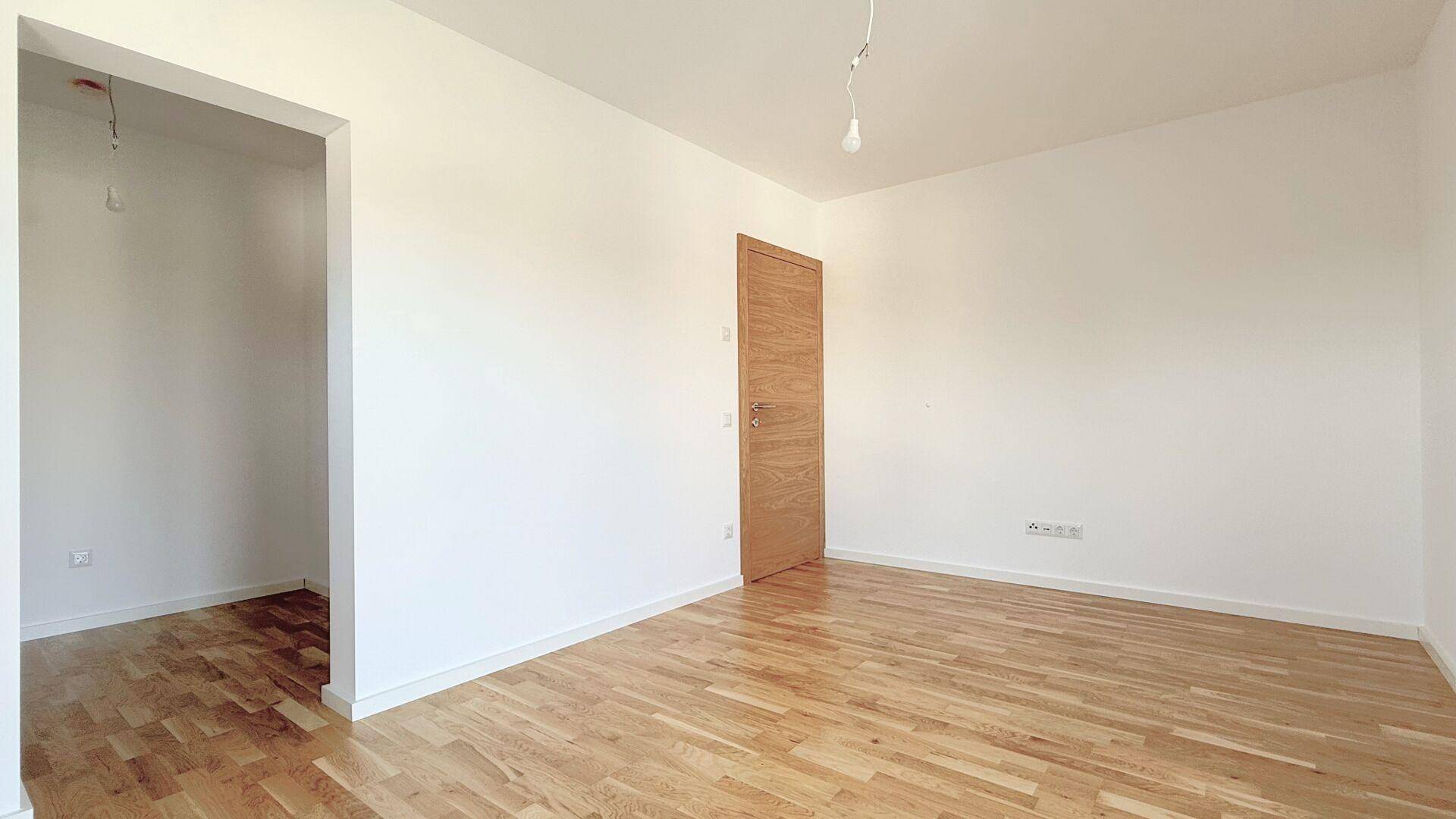 Geräumiges, helles Zimmer mit Parkettboden und offenem Zugang zu einem weiteren Bereich.