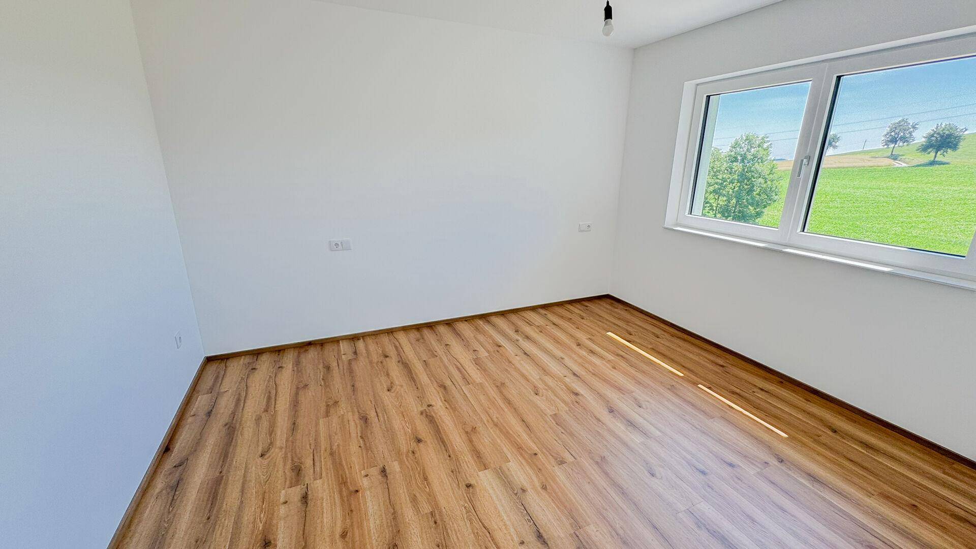 Helles Schlafzimmer mit Laminatboden und einem großen Fenster mit Blick ins Grüne.