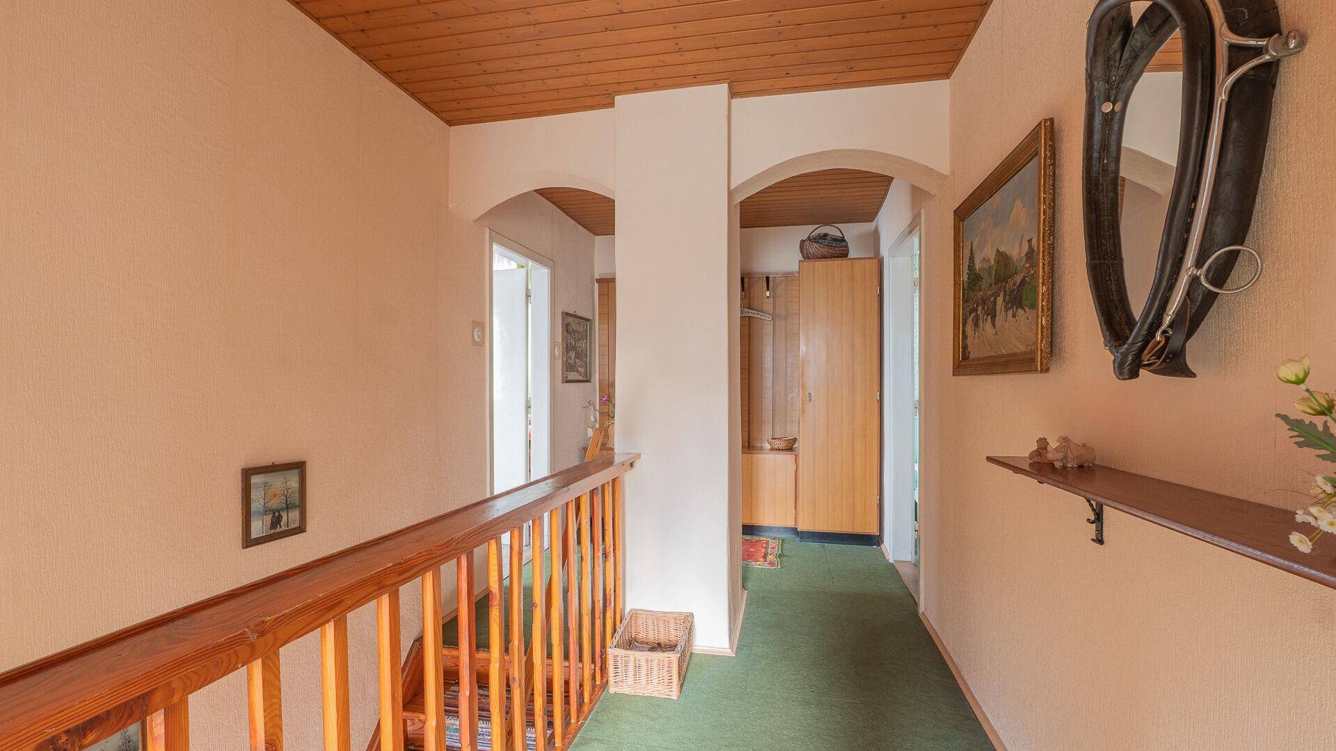 Oberer Flur mit Holzgeländer, Bögen und Teppichboden, führt zu weiteren Zimmern.