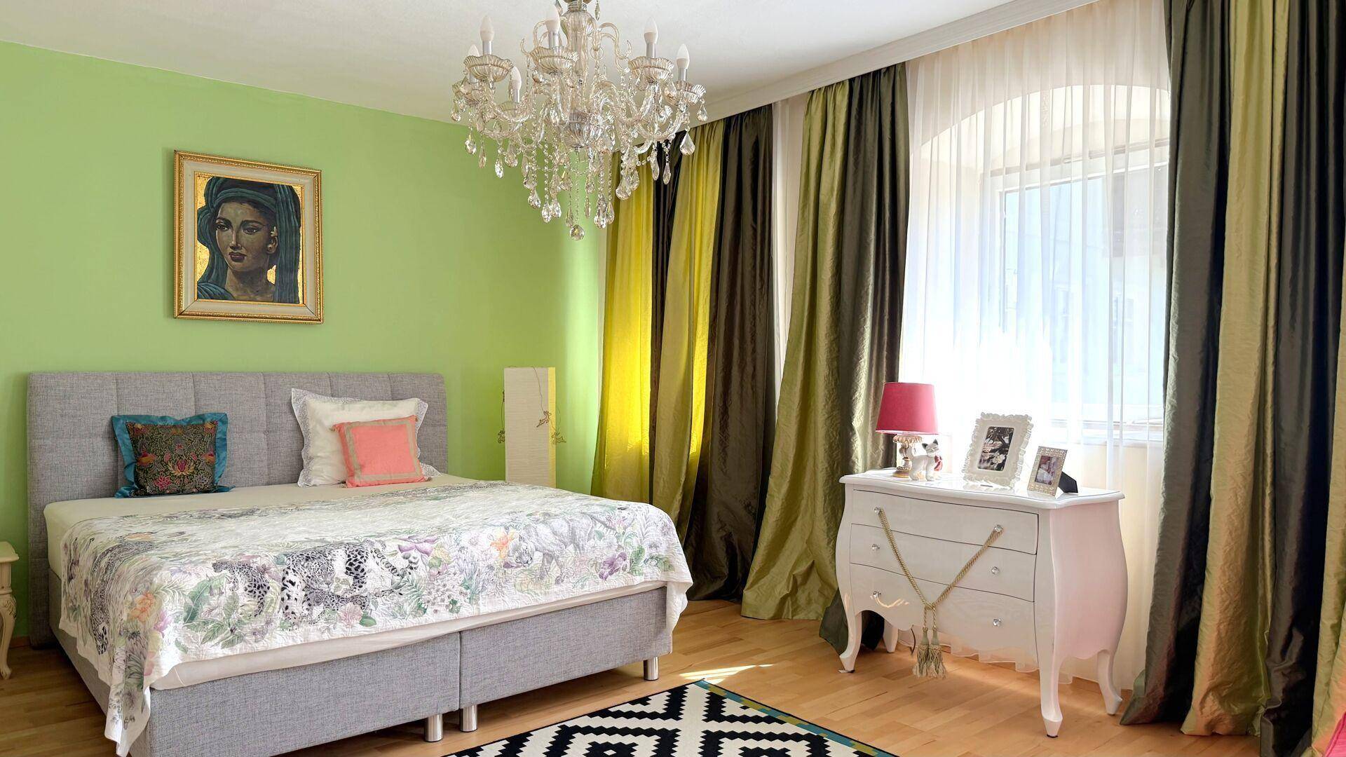 Schlafzimmer mit grünen Wänden, Doppelbett, Kronleuchter und großem Fenster.