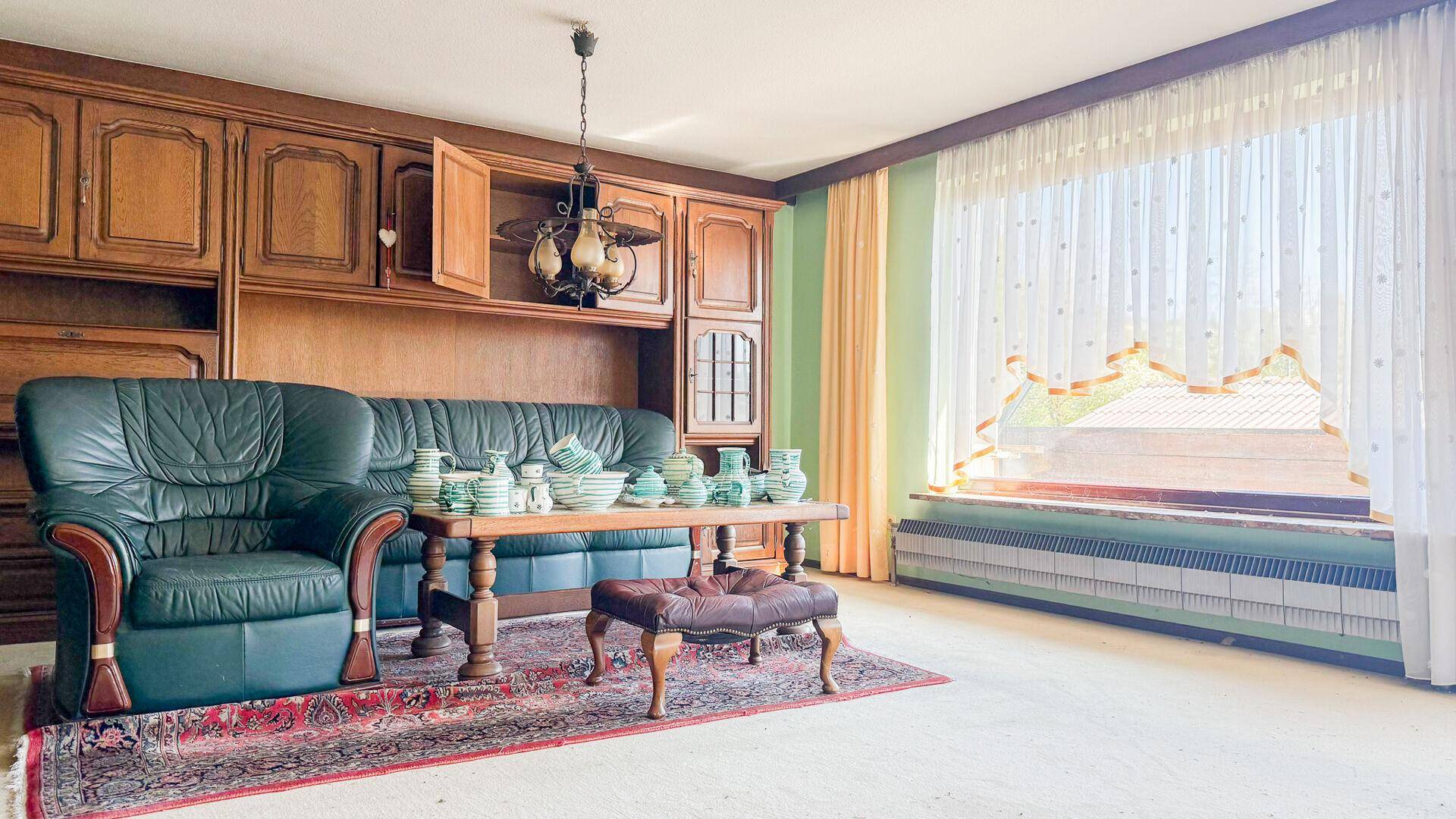 Wohnzimmer mit großer Schrankwand und Ledersofa, gut belichtet durch ein großes Fenster.