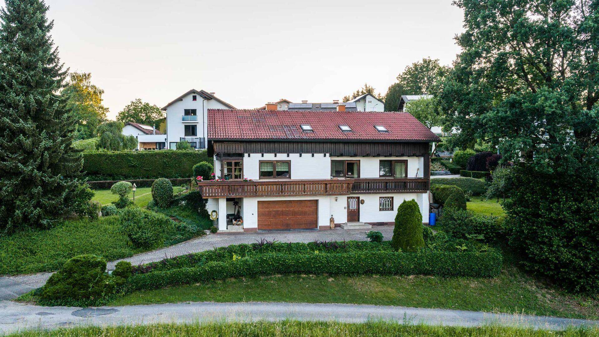 Ansicht eines traditionellen Hauses mit rotem Ziegeldach und Garage, eingebettet in eine grüne Landschaft.