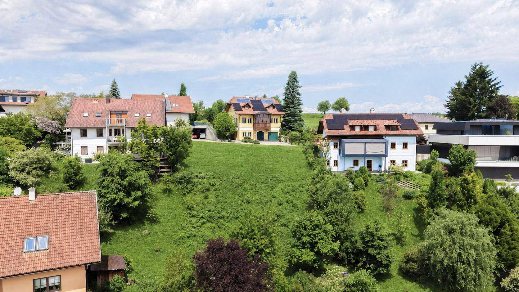 Luftaufnahme einer Wohnsiedlung mit mehreren Häusern an einem grünen Hang, einige mit Solaranlagen.
