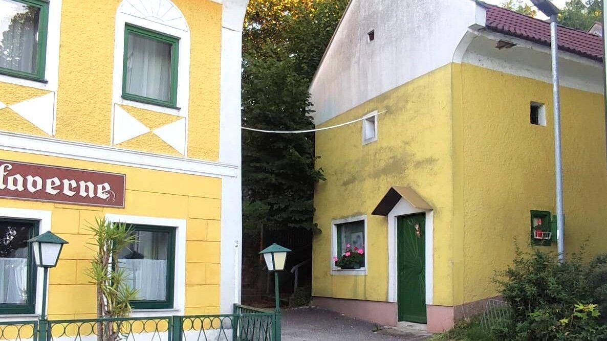 Traditionelle gelbe Gebäude mit grünen Fensterrahmen und Türen, umgeben von Bäumen.