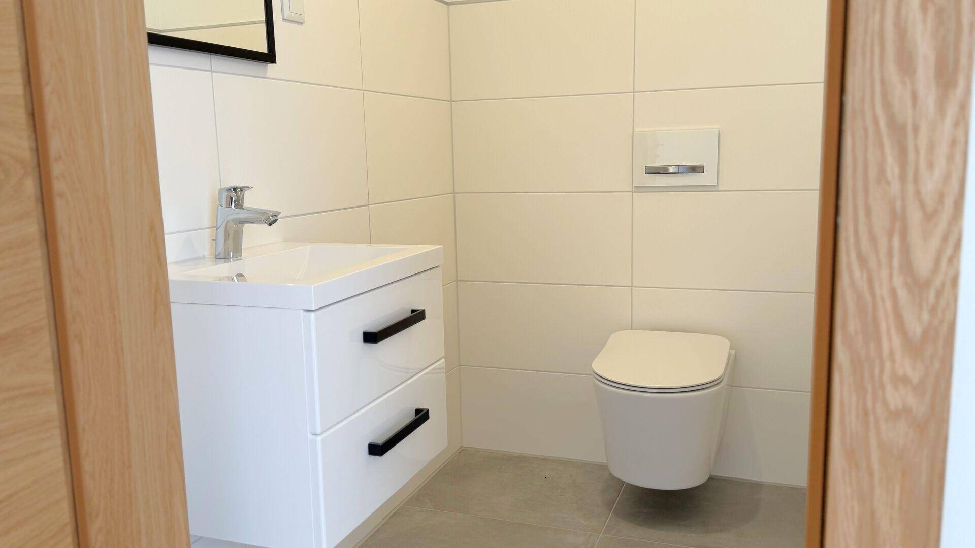Modernes Gäste-WC mit weißem Waschtischunterschrank, Wand-WC und hellen Fliesen.