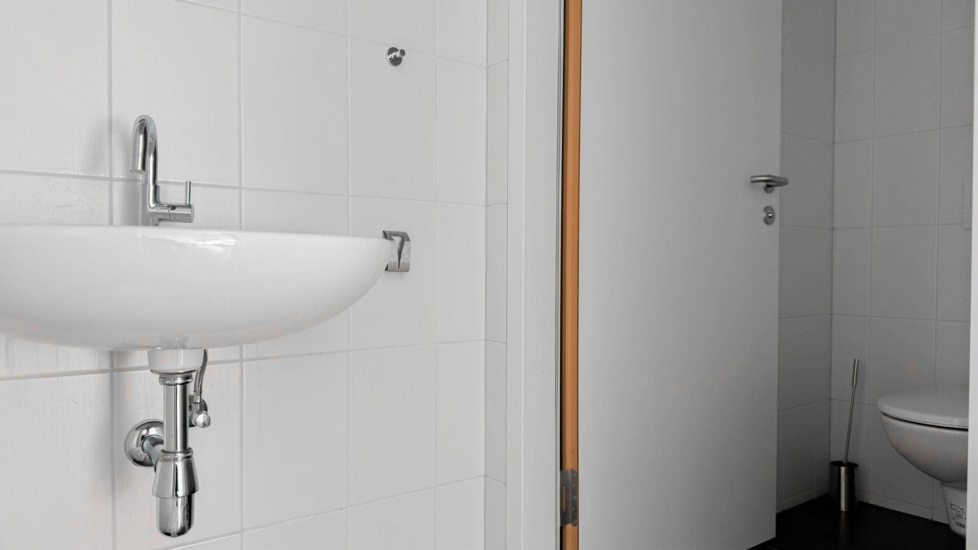 Modernes Badezimmer mit weißem Waschbecken und Fliesen an den Wänden, das sauber und funktional ist.