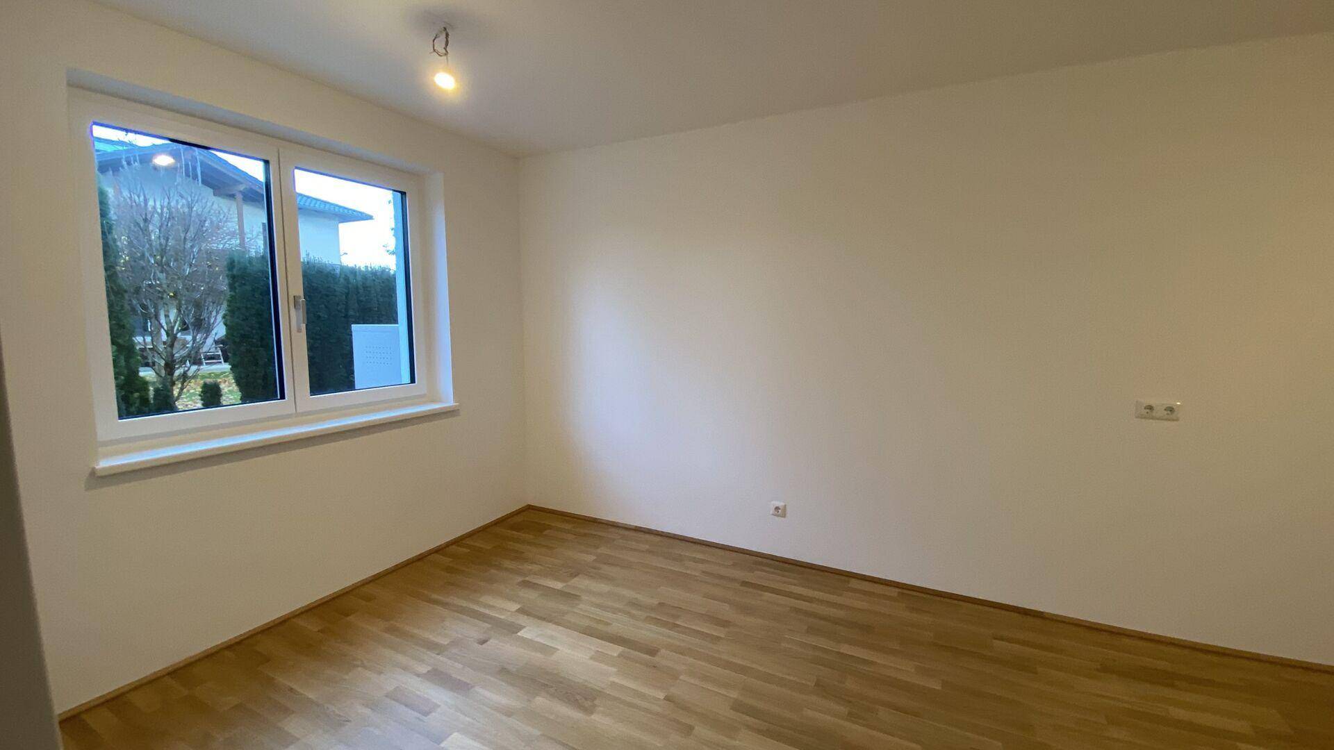Helles Zimmer mit Parkettboden und großem Fenster, ideal als Schlaf- oder Arbeitszimmer.