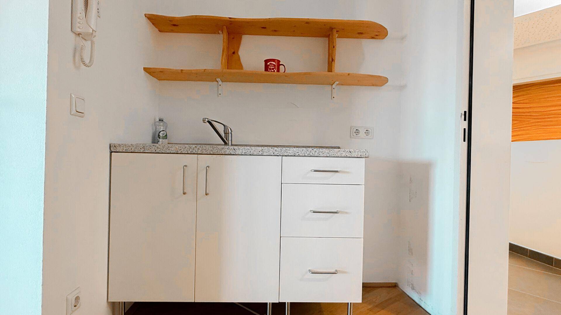 Kleine Küchenzeile mit Spüle, Unterschränken und rustikalen Holzregalen an der Wand.