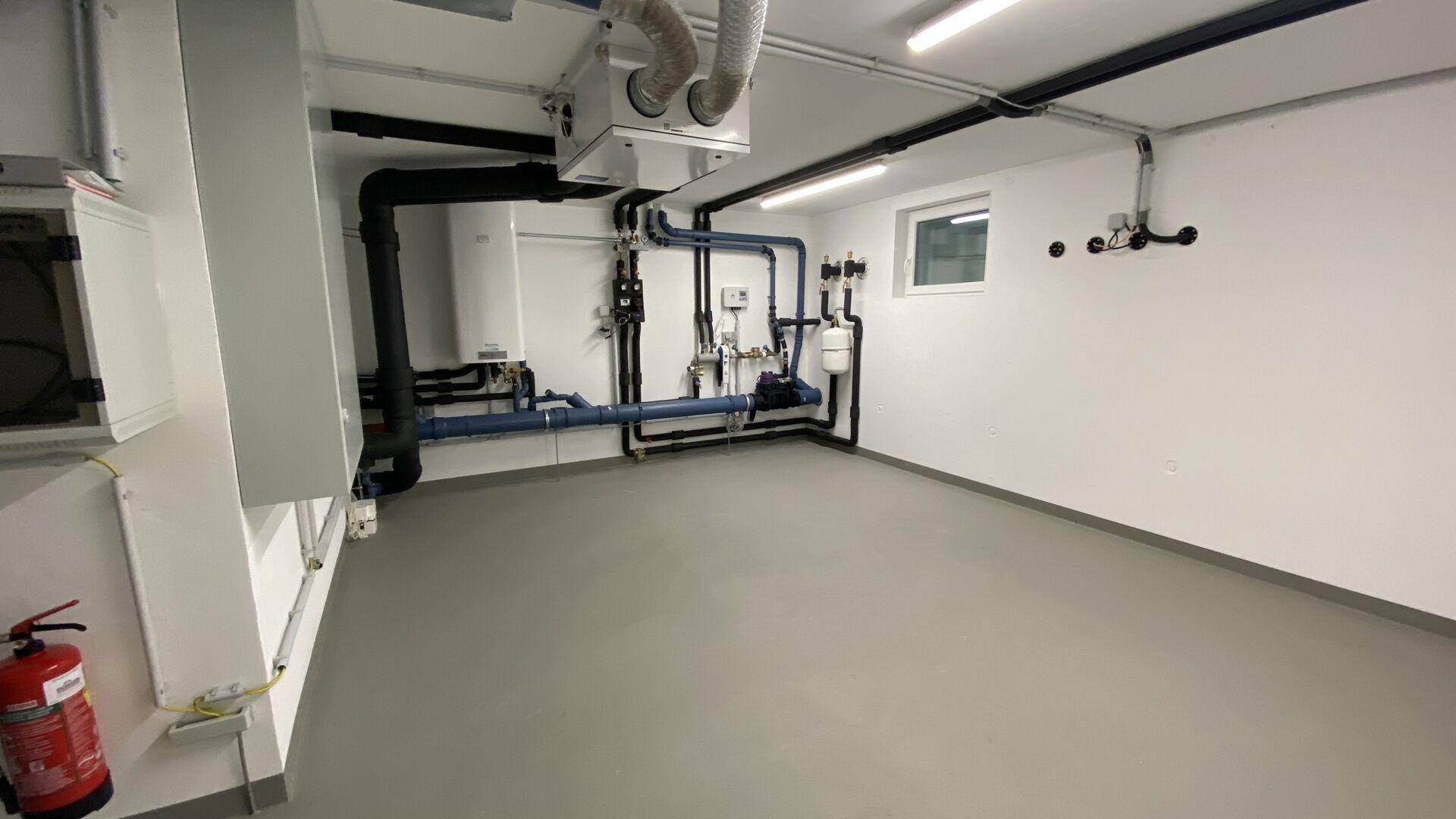 Technikraum im Keller mit Heizungsanlage, Lüftungssystem und zahlreichen Leitungen.