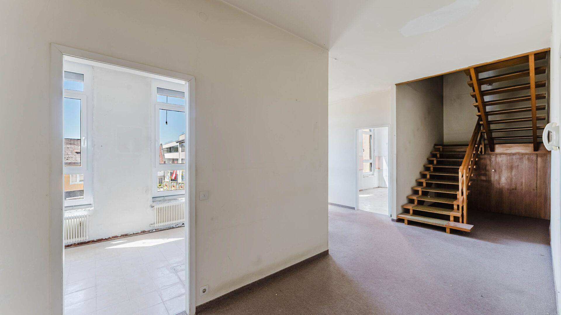 Heller Flur mit Holztreppe und Zugang zu weiteren Räumen, bereit zur Renovierung.